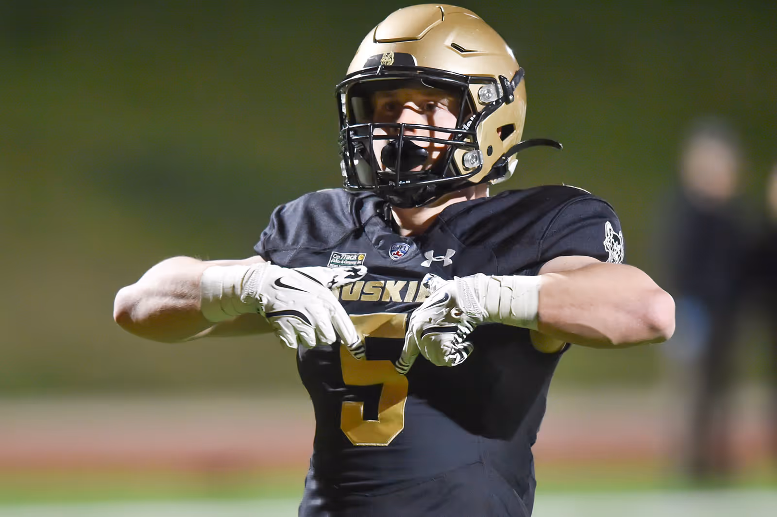 Football player in black and gold Huskies uniform celebrating on field at night.