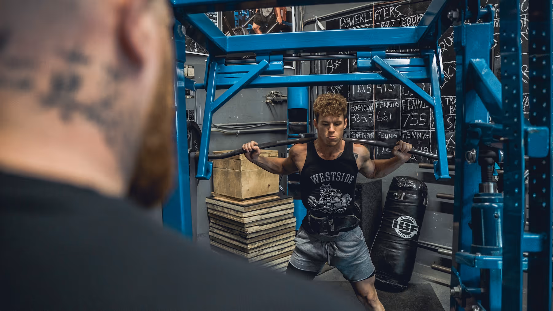 Young man in a weightlifting belt performing a squat with a barbell on his shoulders in a gym.