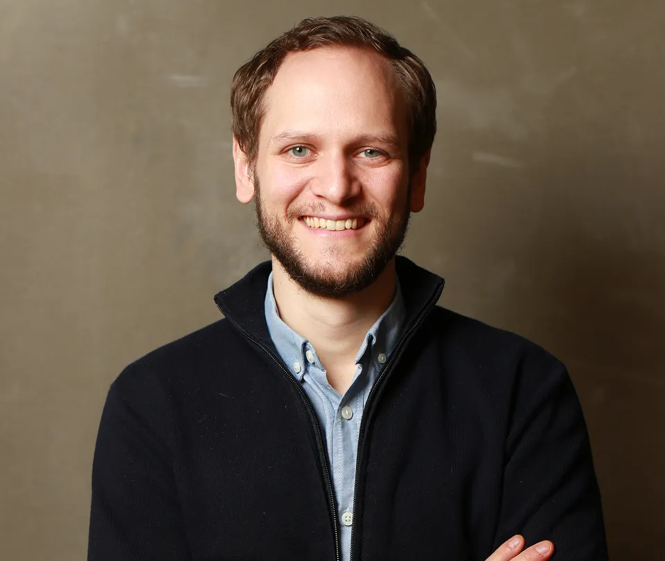 Bearded man in a navy sweater over a light blue shirt, arms crossed, studio portrait for Workpath.