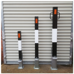 Three black and white removable bollards of different heights installed on a concrete surface in front of a closed gray metal roller door.