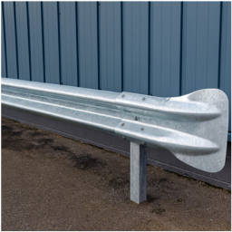 Close-up of a galvanized steel guardrail mounted on a post beside a paved surface with a blue metal wall in the background.