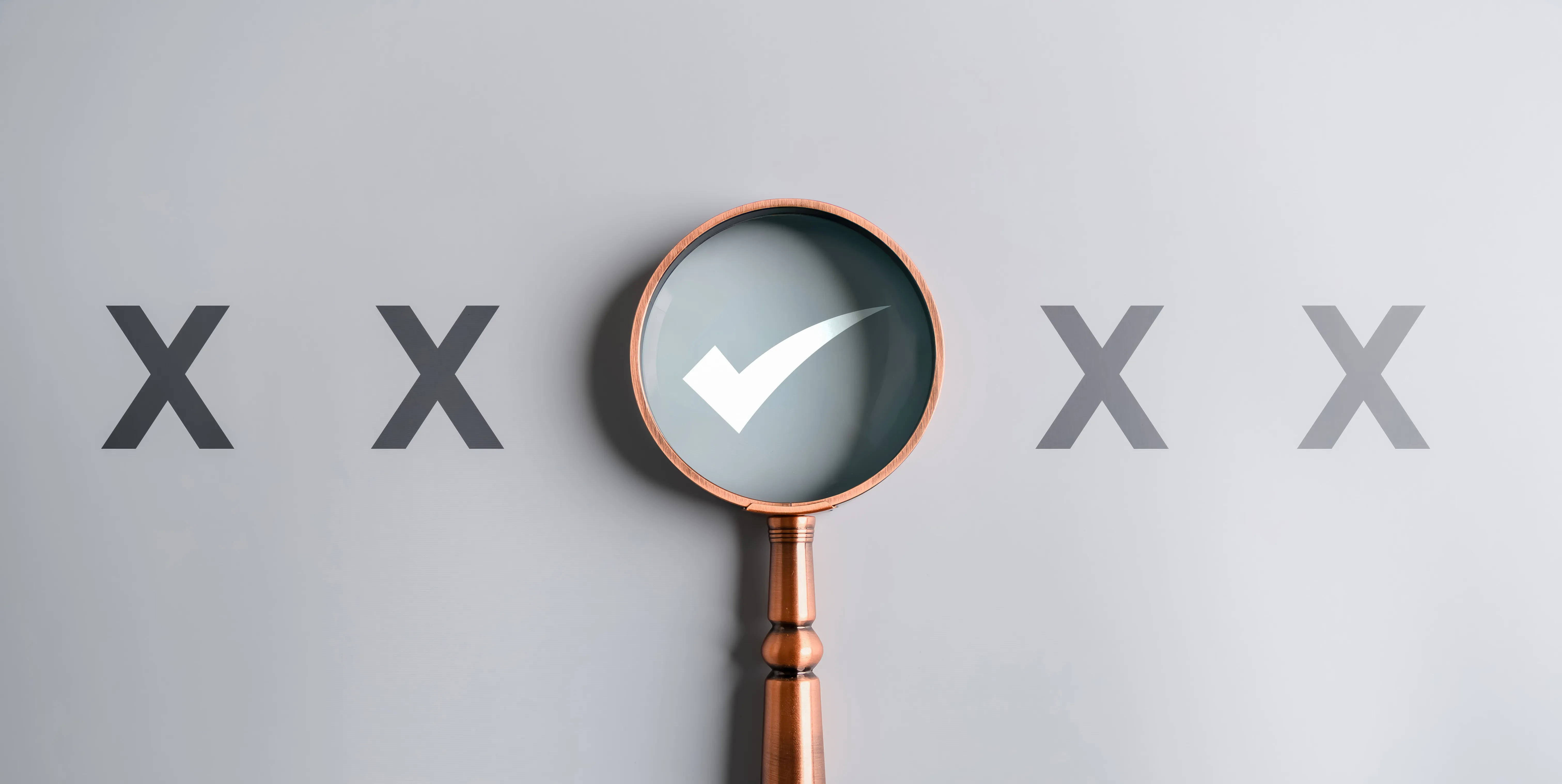 Magnifying glass highlighting a white check mark among four black X marks on a gray background.