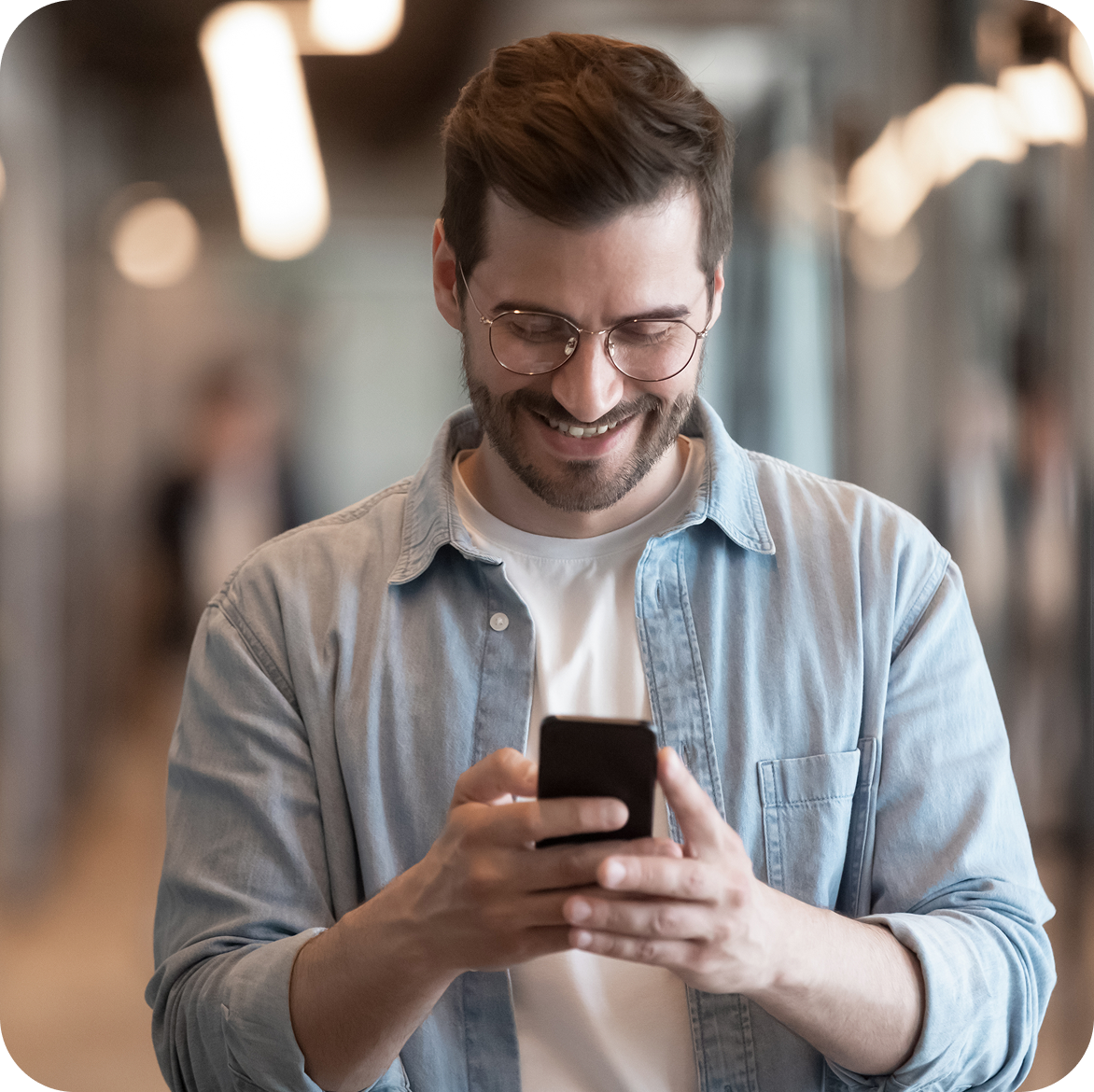 Smiling man in a denim shirt looking at his phone