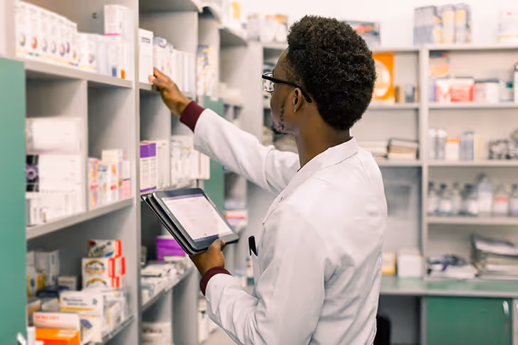 Pharmacist getting item off shelf with tablet in hand