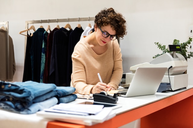 Business retail owner reviewing online payment transactions alongside a till at a fashion store