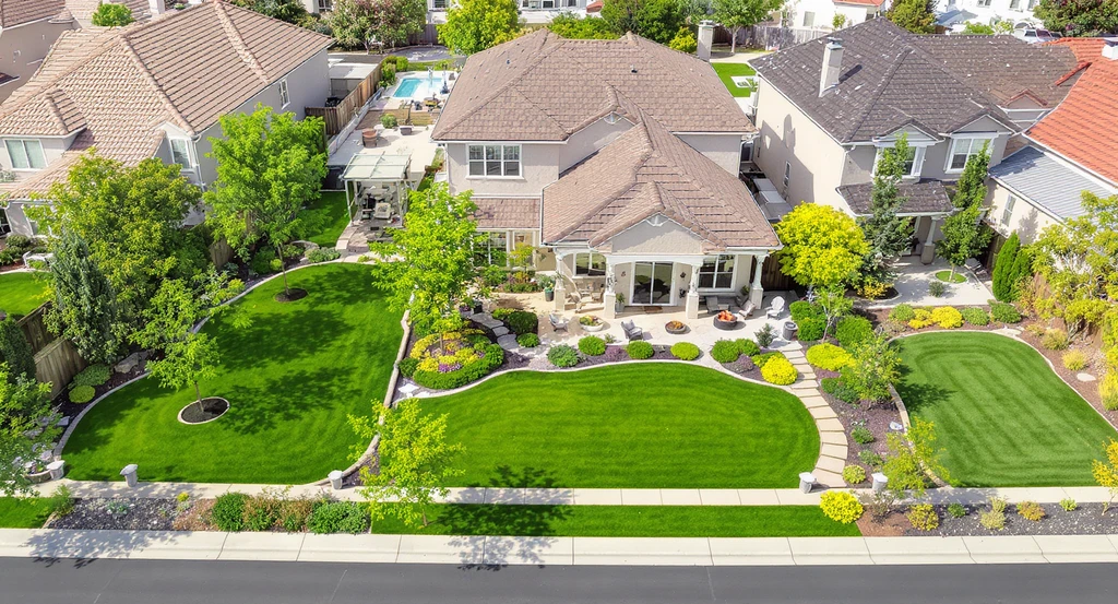 Aerial view of a home’s backyard showing landscaping upgrades: lush lawns and trees for curb appeal, outdoor living and edible garden for high return on investment, and sustainable native planting for cost-effective value.