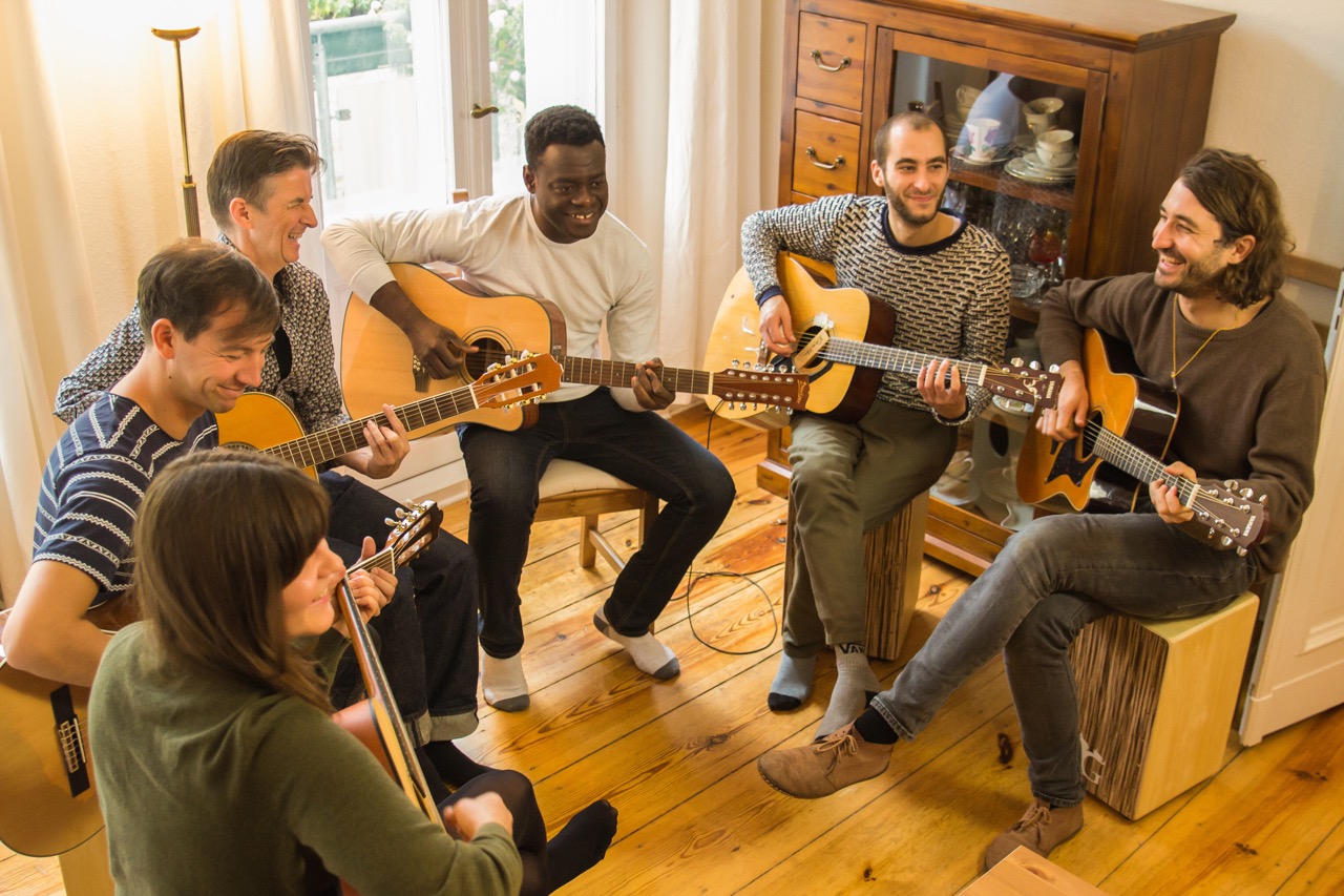 Erwachsene beim Gitarrenunterricht in einer Gruppe im Wohnzimmer in Berlin.