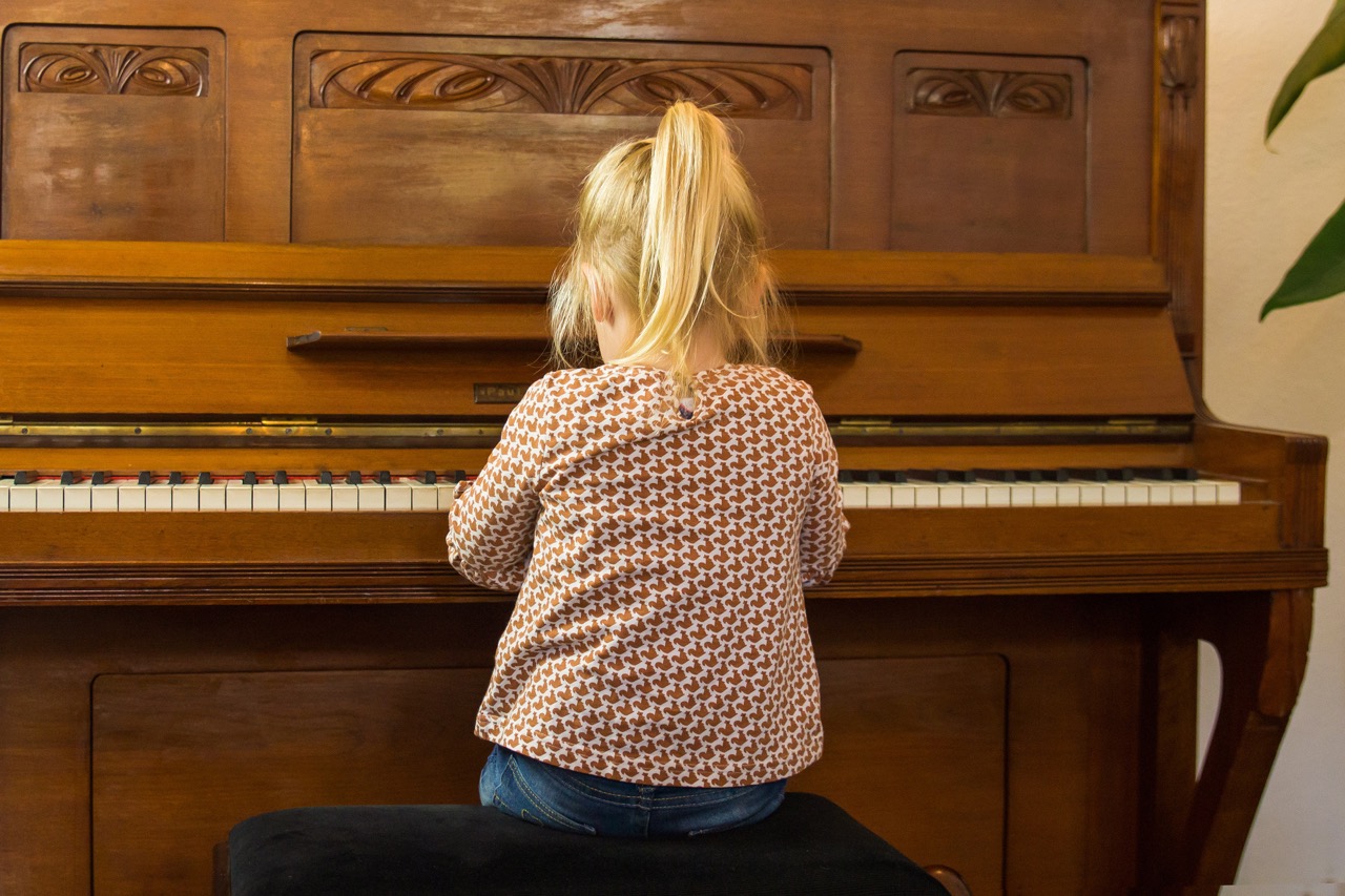 Kleines Mädchen sitzt beim Klavierunterricht in Berlin Friedrichshain im Wohnzimmer und spielt Klavier