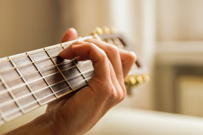 Eine Hand greift einen Akkord auf dem Griffbrett einer Gitarre.