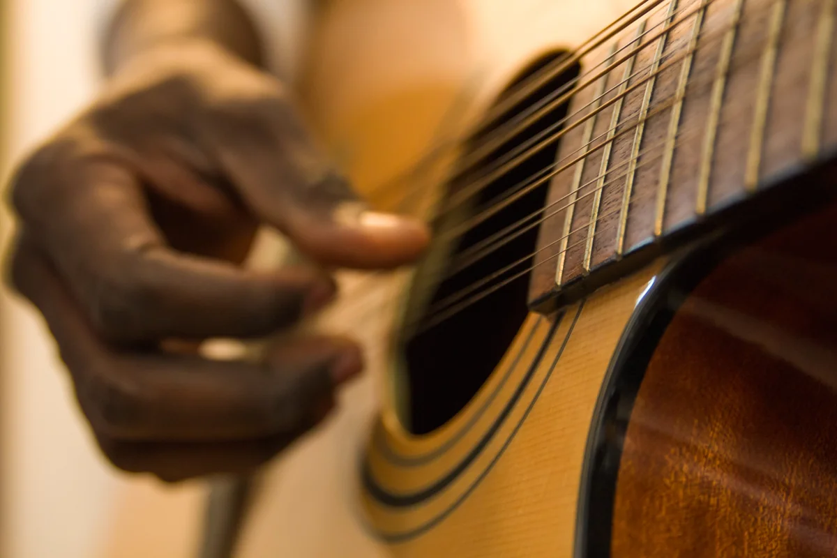 Nahaufnahme einer Hand beim Anschlagen der Saiten einer akustischen Gitarre.