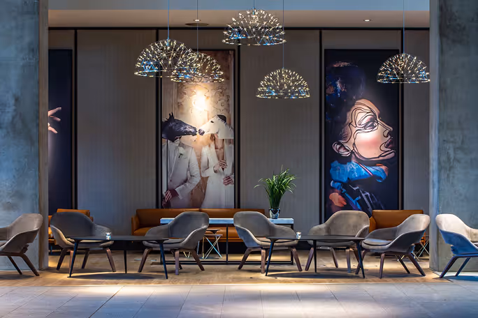 Modern lounge with gray chairs, brown sofas, abstract art portraits, and hanging dome-shaped lights.
