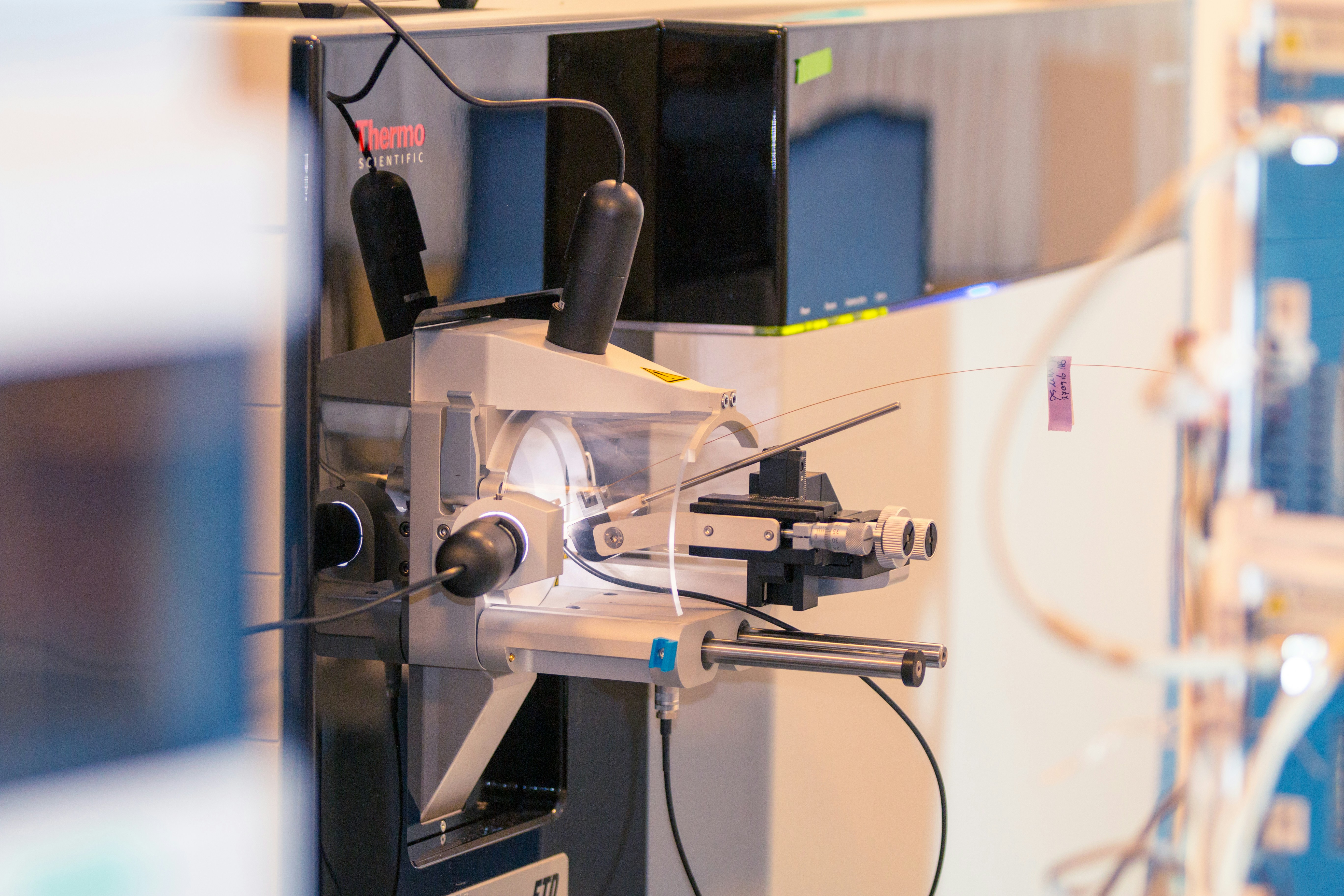 Close-up of a materials testing instrument holding a thin fiber sample on a precision positioning stage.