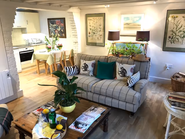 Cozy living room with gray sofa, plants, botanical art, and open kitchen