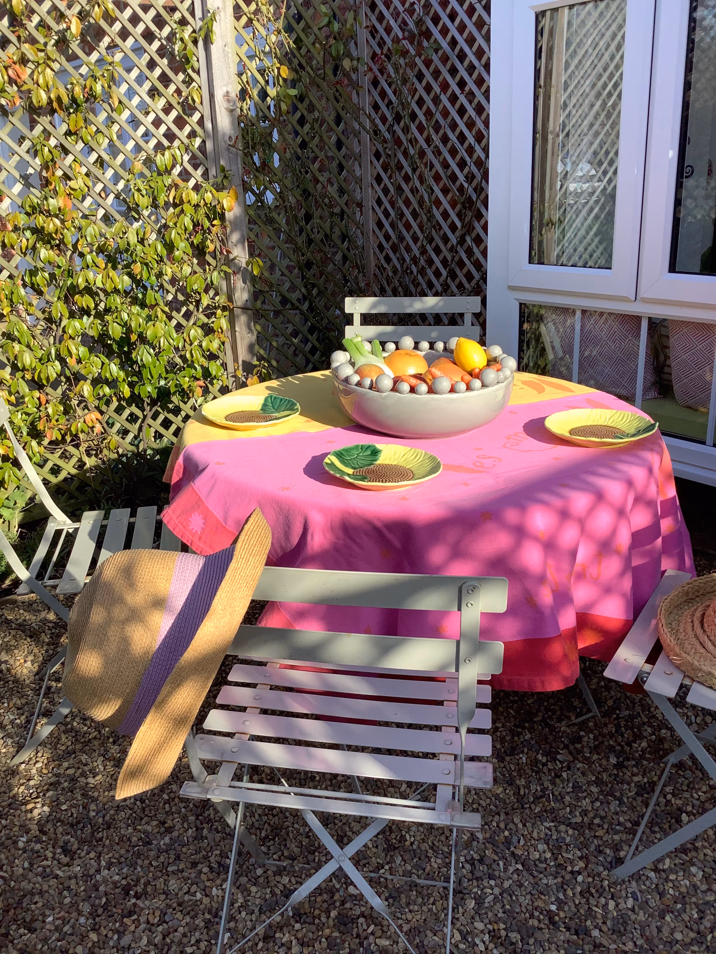 Outdoor table with pink tablecloth, fruit bowl, and folding chairs in garden