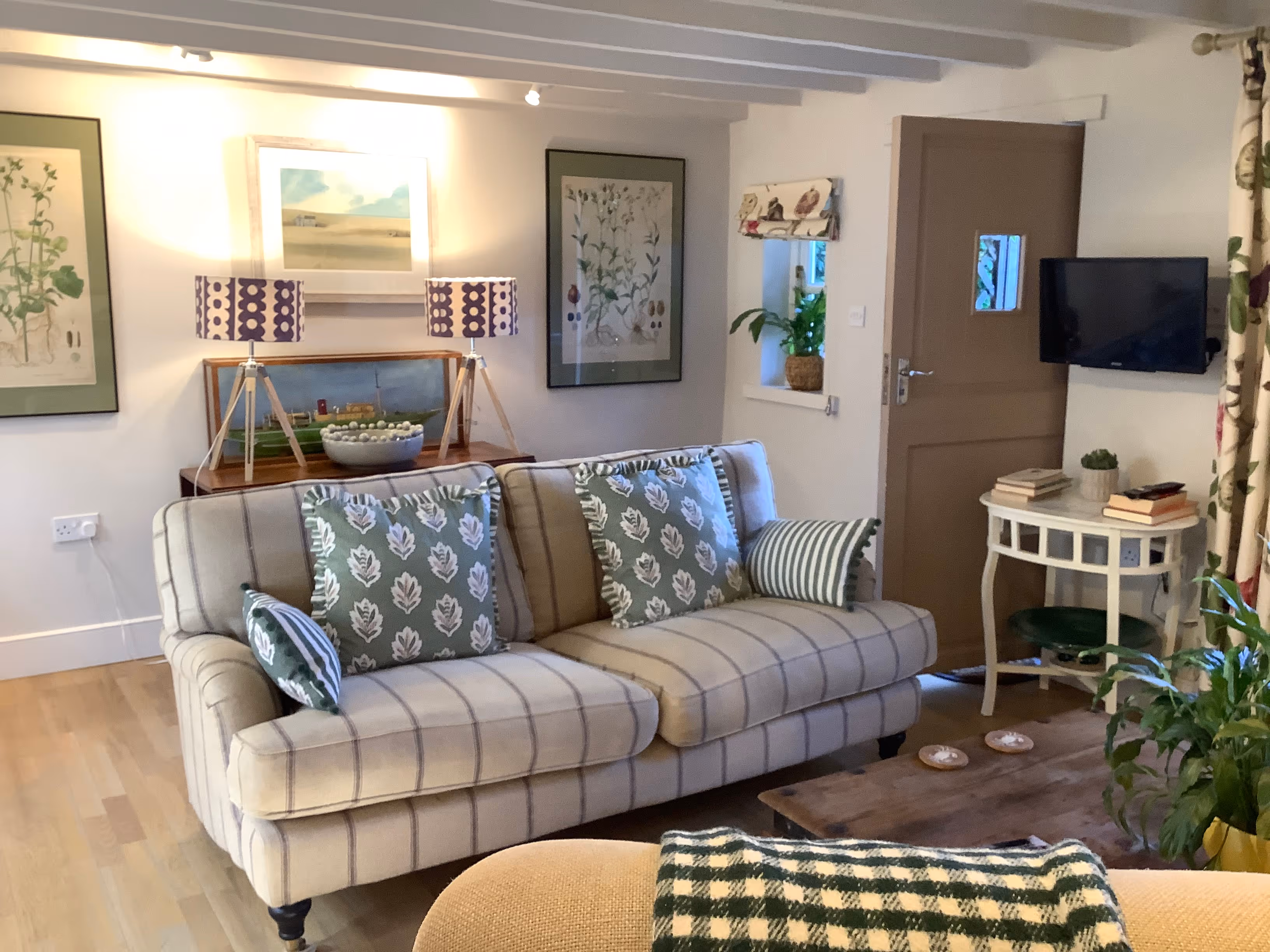 Cozy living room with striped sofa, botanical art, and tripod lamps