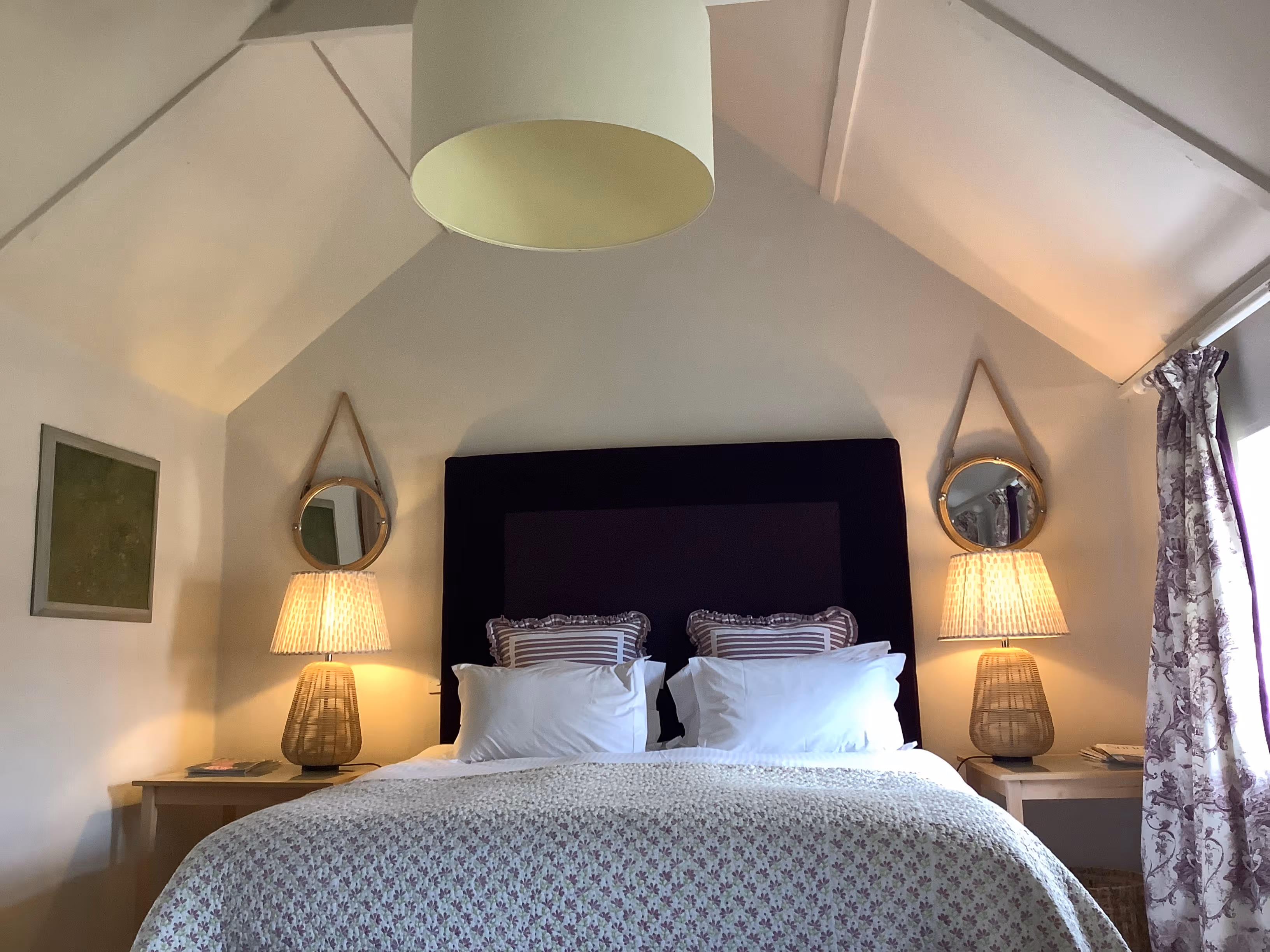 Cozy bedroom with black headboard, woven lamps, and circular mirrors