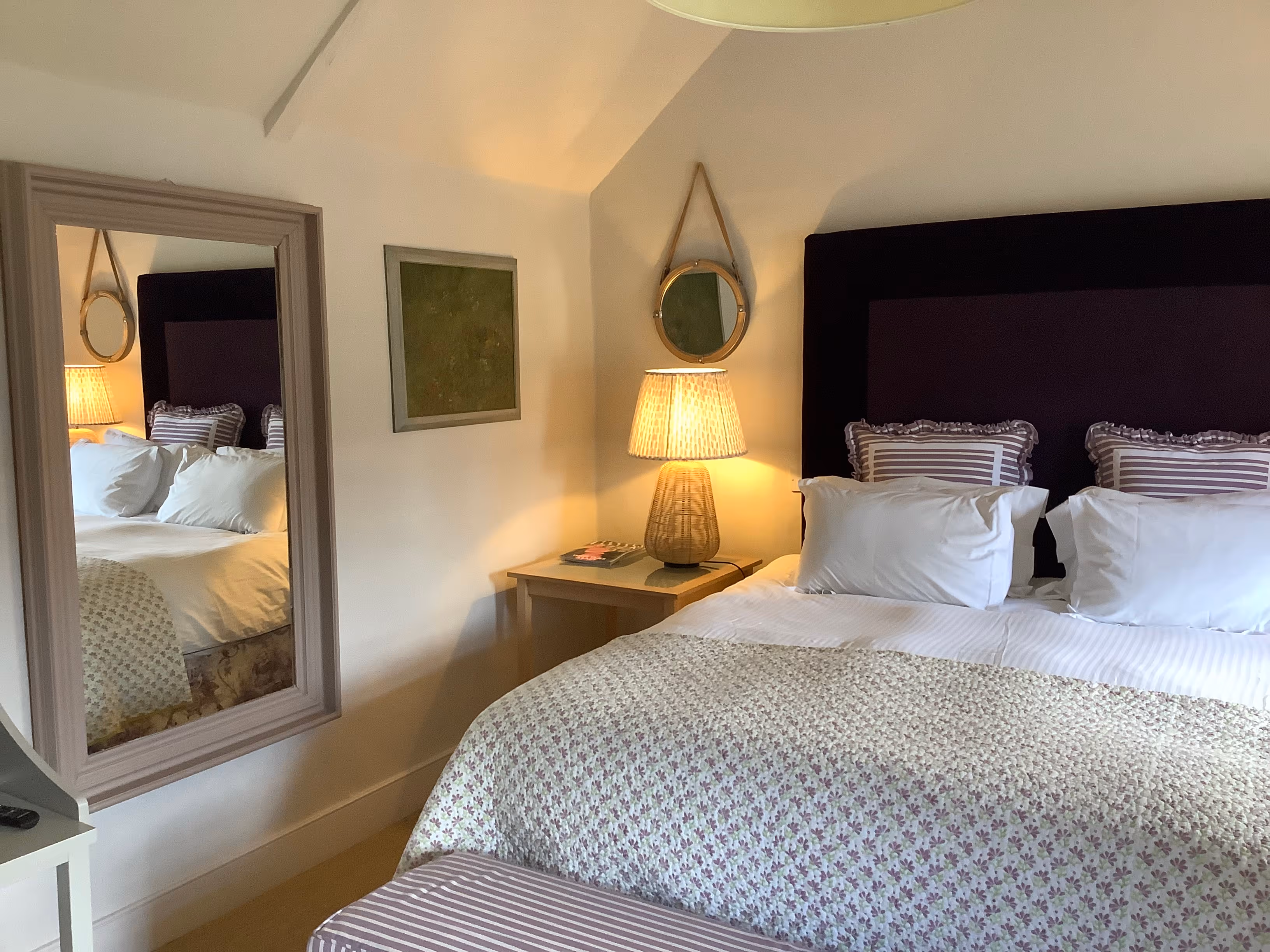 Cozy bedroom with white bedding, mirror, lamp, and black headboard