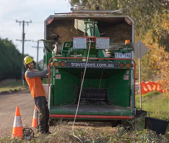 Worker smiling beside a wood chipper with safety cones on a rural roadside.