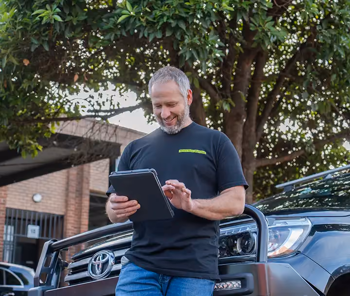 Man using a tablet while leaning on a Toyota truck.