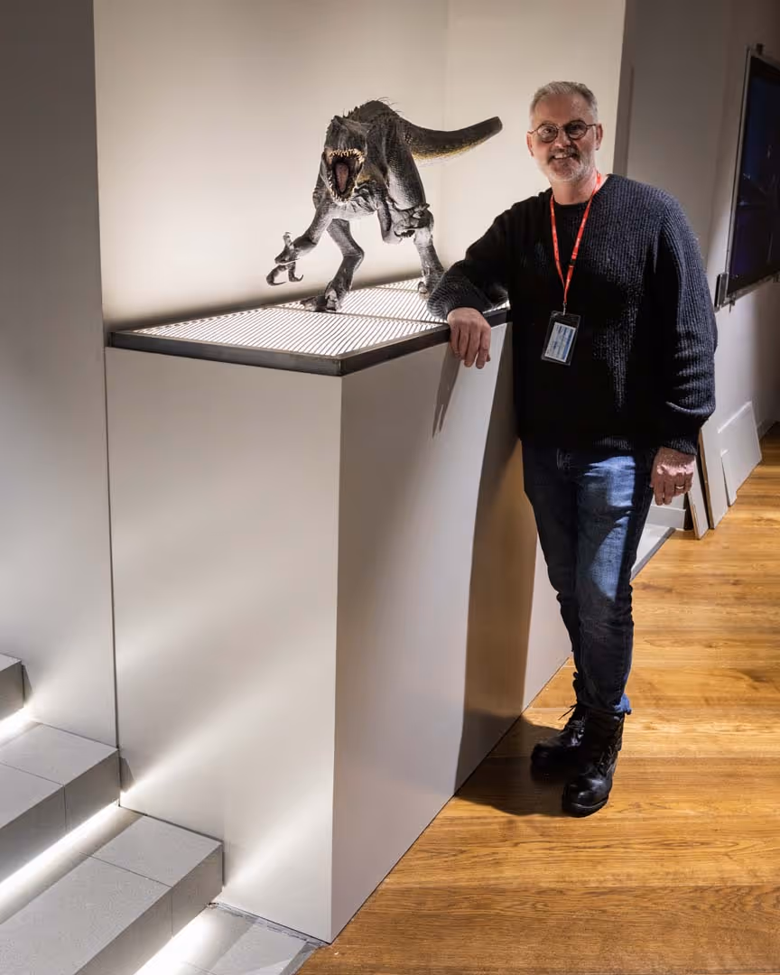 A man stands next to a dinosaur model on a display podium.