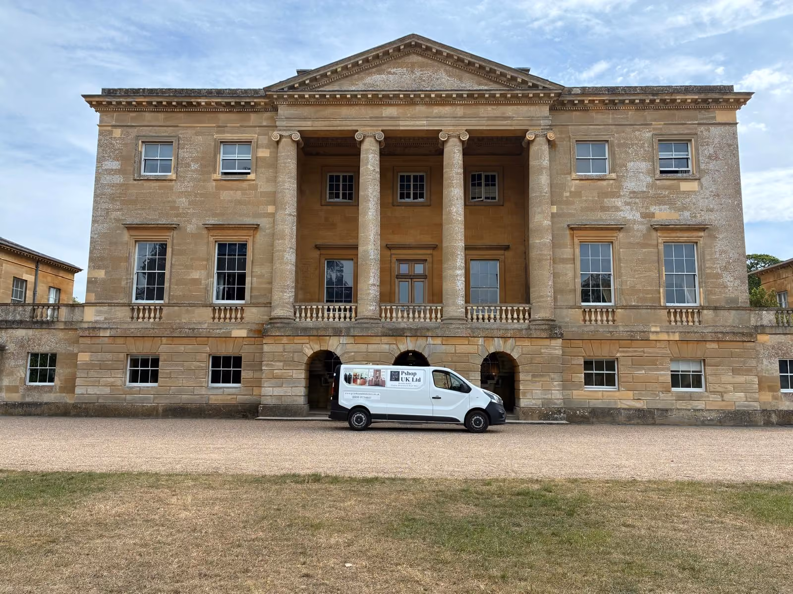 A white van parked in front of a large, historic stone building with tall columns.