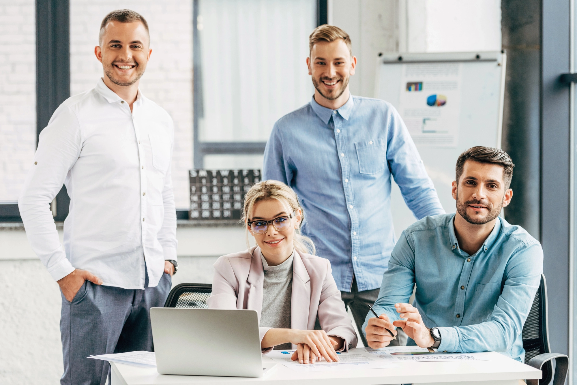 A diverse group of professionals collaborates at a desk, engaged in discussion with a laptop and documents in a modern office setting