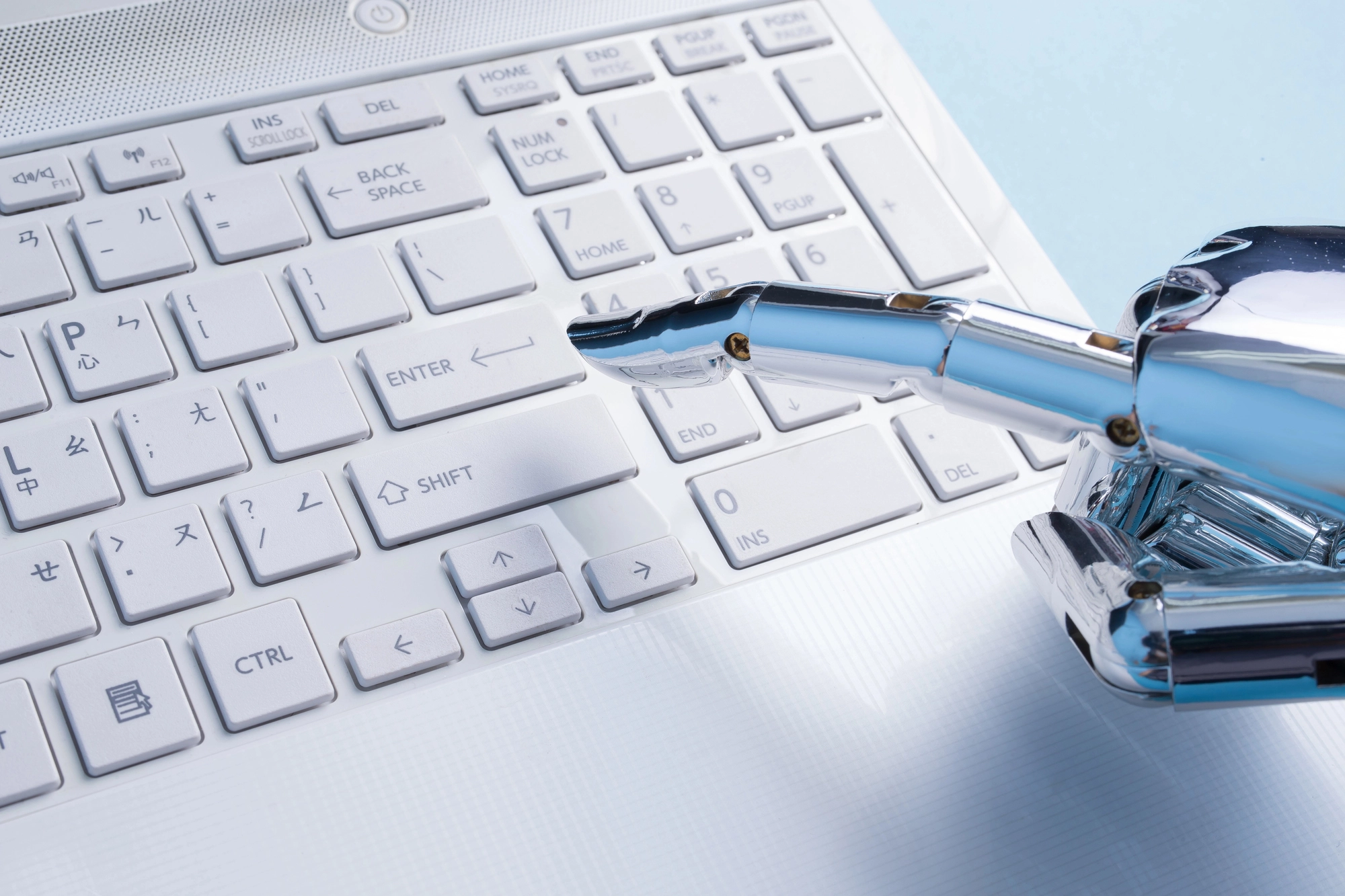 A metallic robotic hand poised over a white laptop keyboard, highlighting the keys and a modern, sleek design