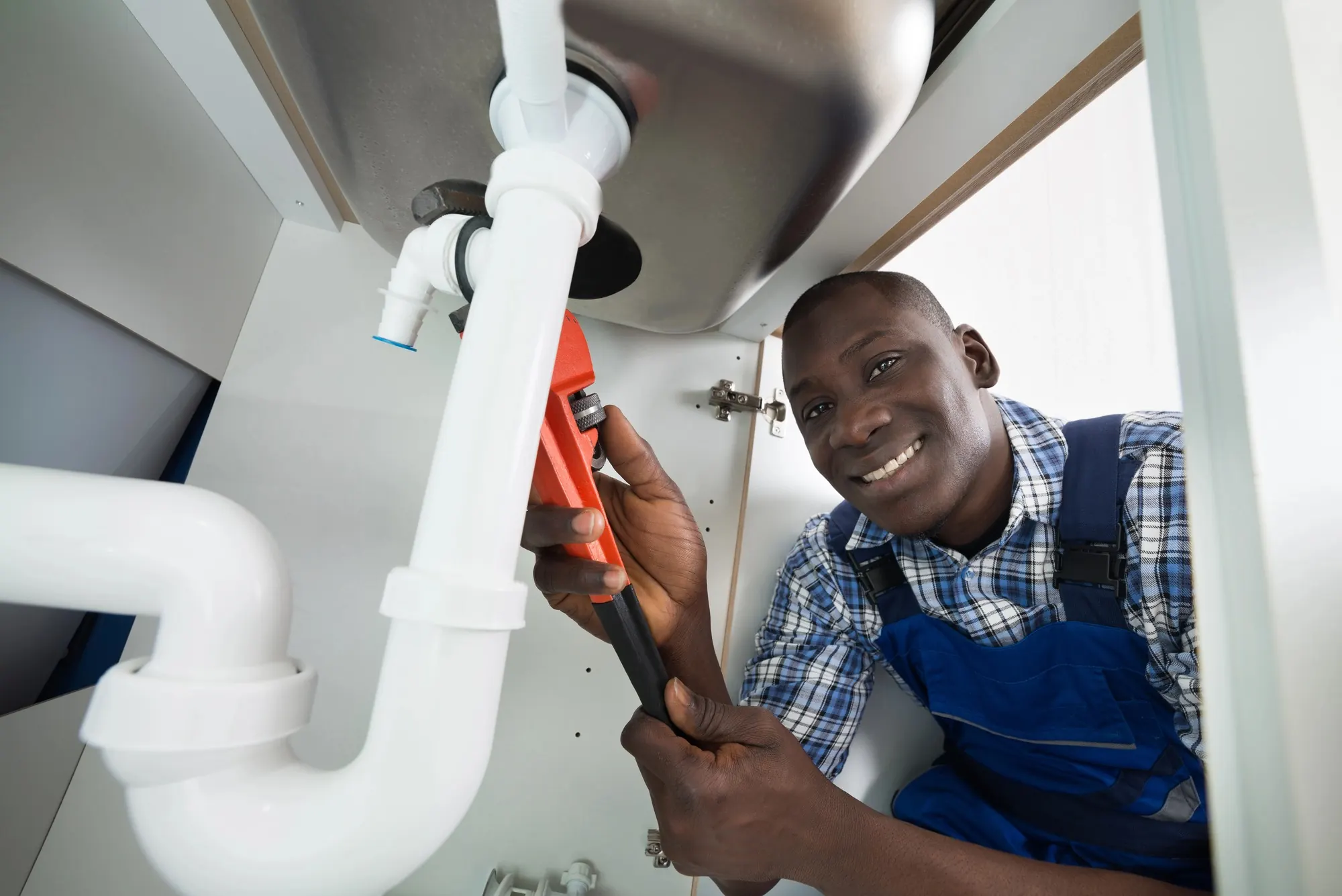 Professional plumber repairing plumbing beneath a kitchen sink, representing lead generation for plumbing services and home repair solutions