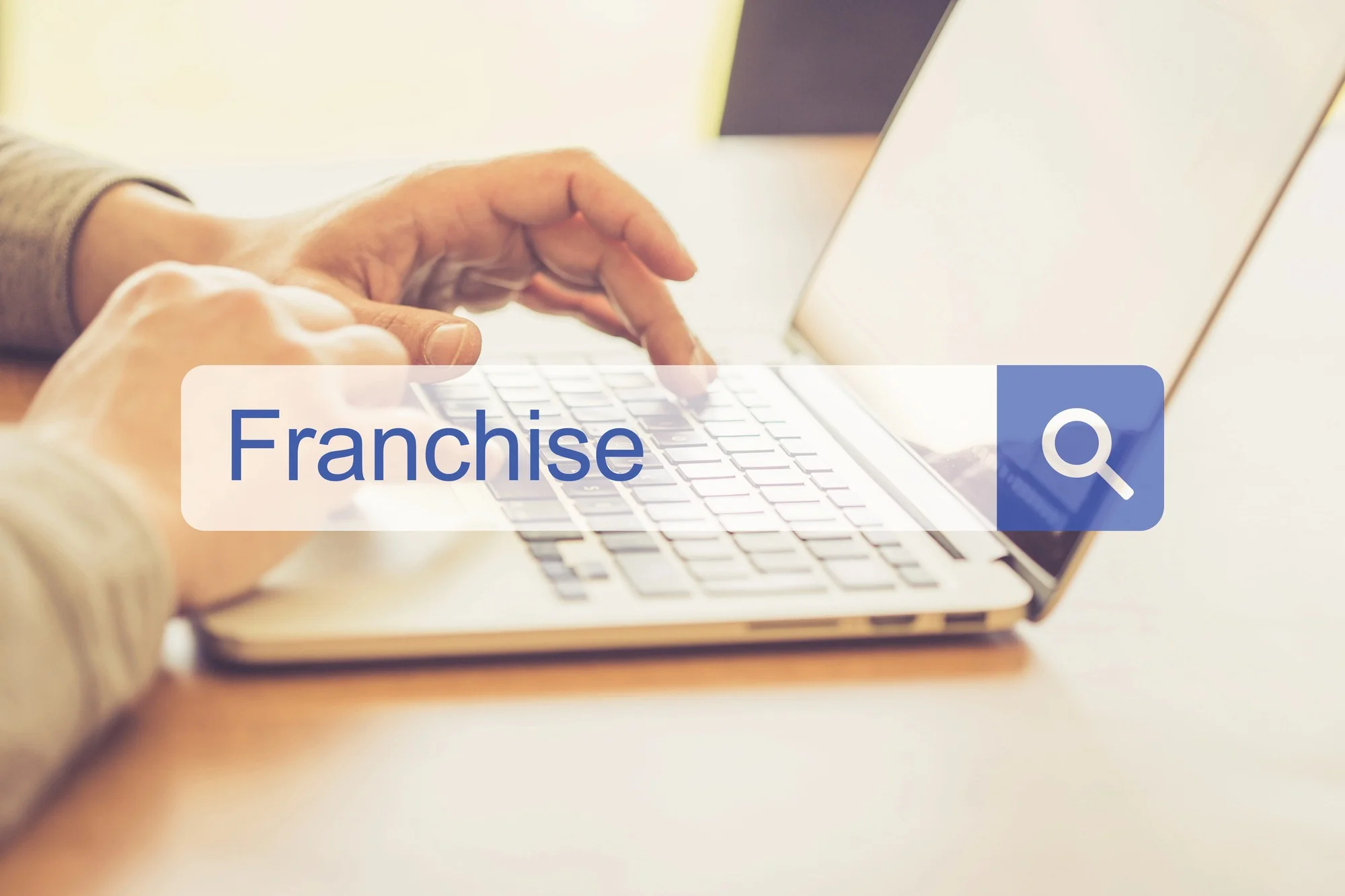 Close-up of hands typing on laptop with search bar showing 'Franchise'