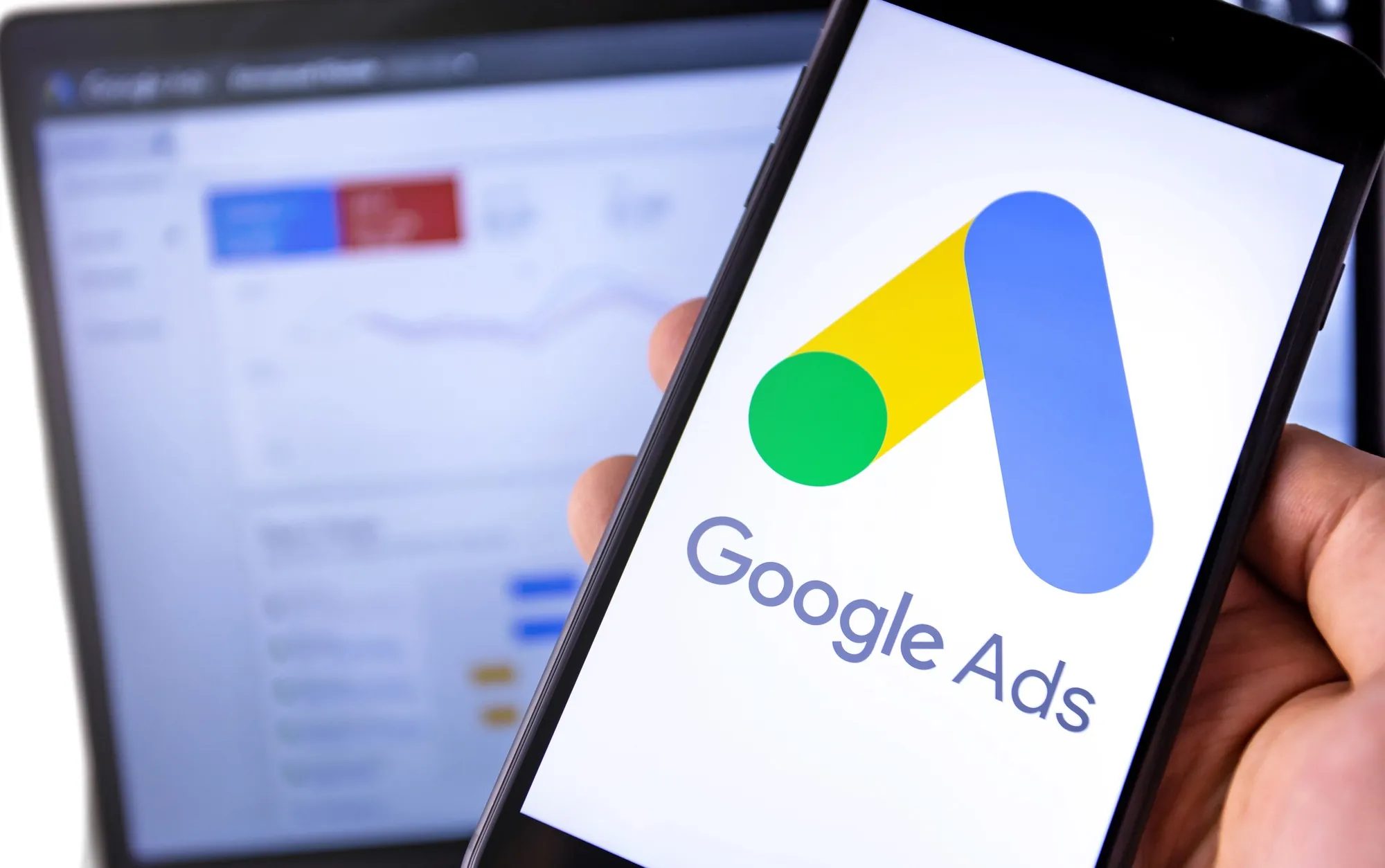 Close-up of the Google Ads logo on a smartphone with an advertising dashboard in the background