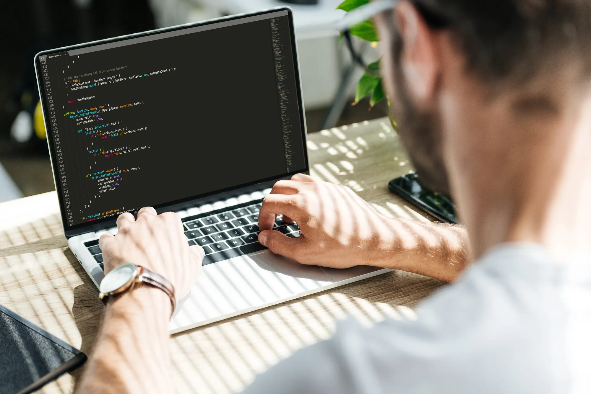 Over-the-shoulder view of a developer typing code on a laptop displaying JavaScript syntax