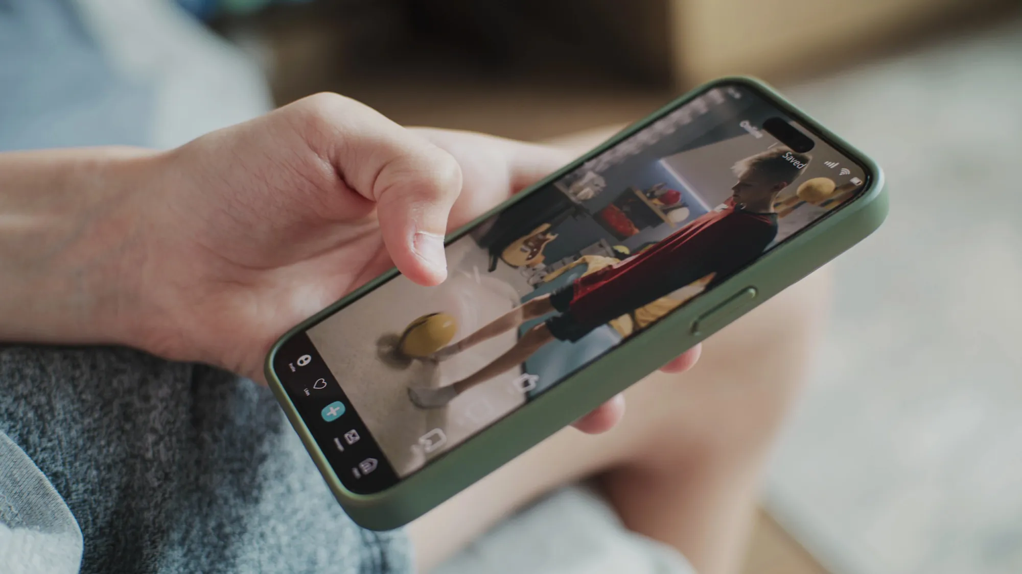 Hand holding a smartphone showing a short video app with a person in a red cape performing in a bedroom