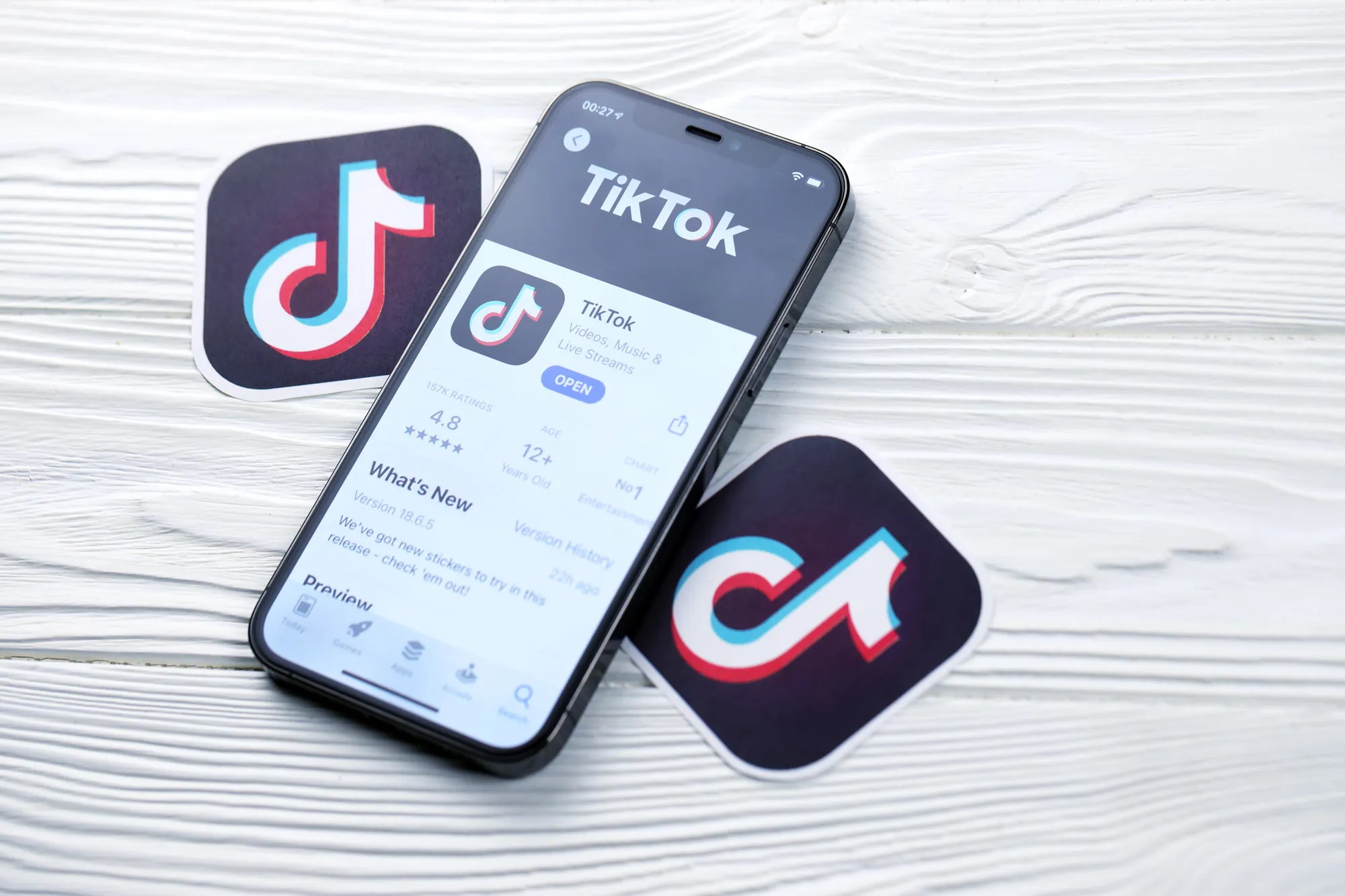 Smartphone displaying the TikTok app store listing next to TikTok logo stickers on a wooden surface