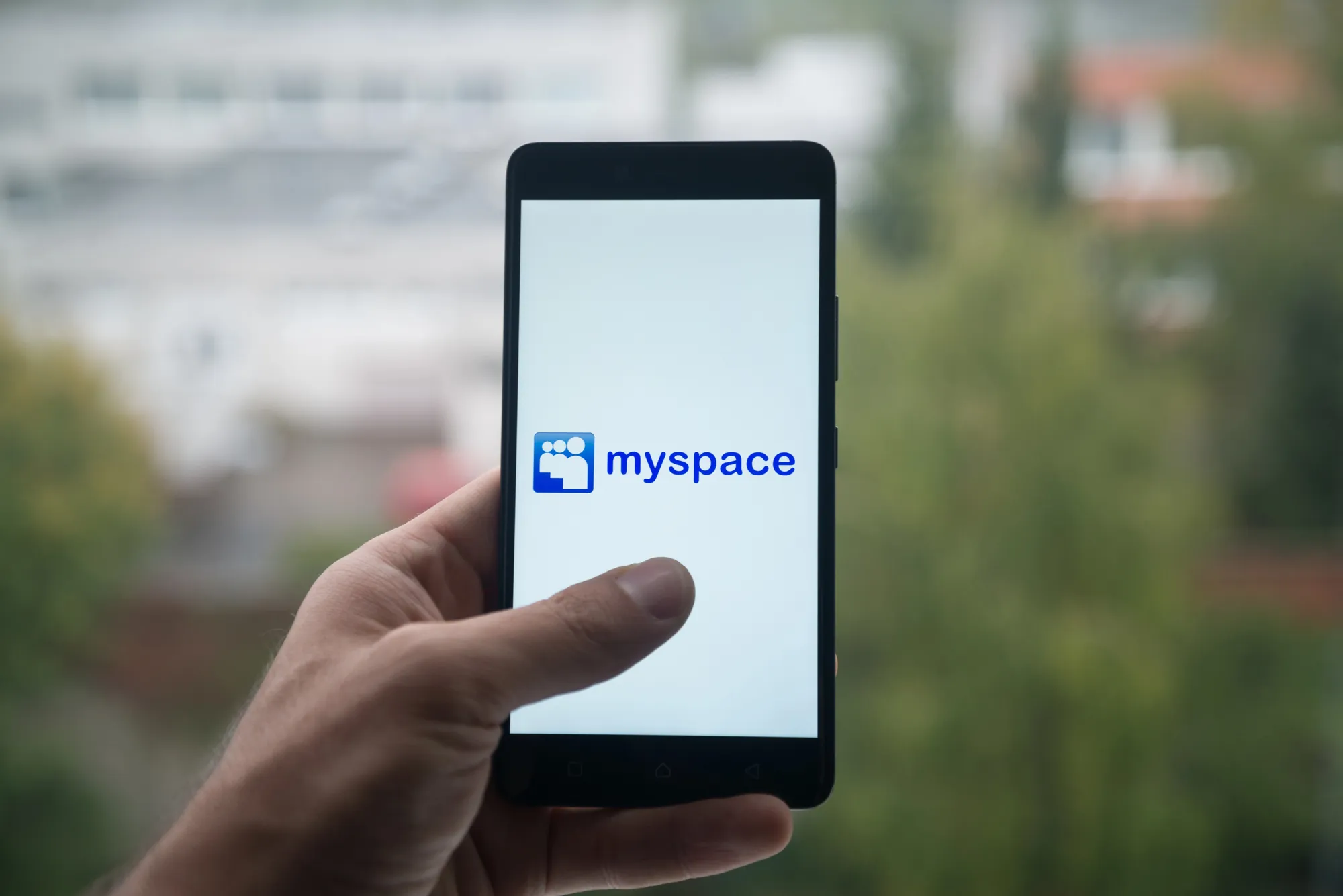 Hand holding a smartphone displaying the MySpace app logo and name against a blurred outdoor background