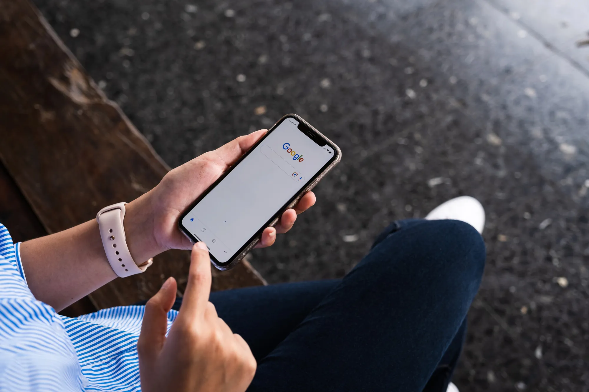 Overhead view of a person using a smartphone to perform a Google search while sitting outdoors