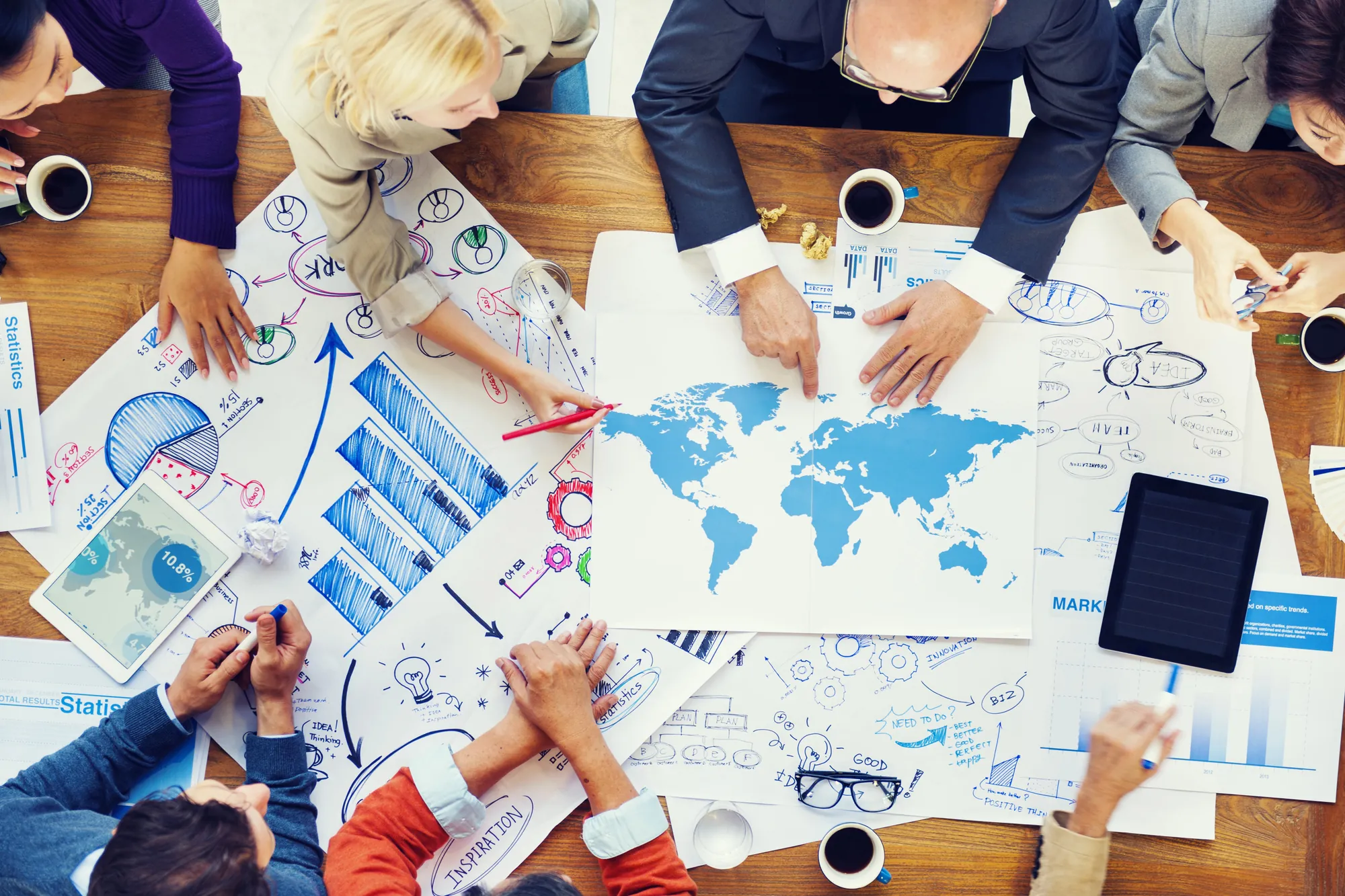 Overhead view of a business team brainstorming global strategy with hand-drawn charts, a world map, and sticky notes on a table