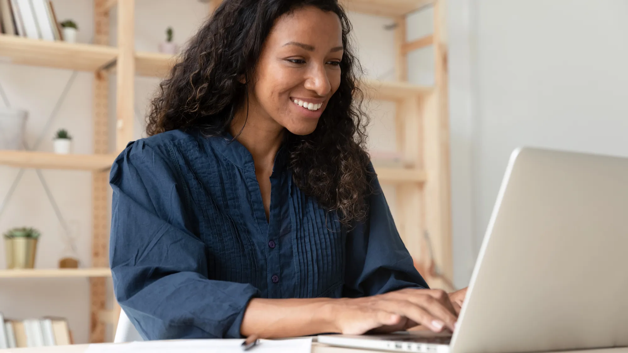 Smiling woman typing on a laptop at a desk in a bright home office