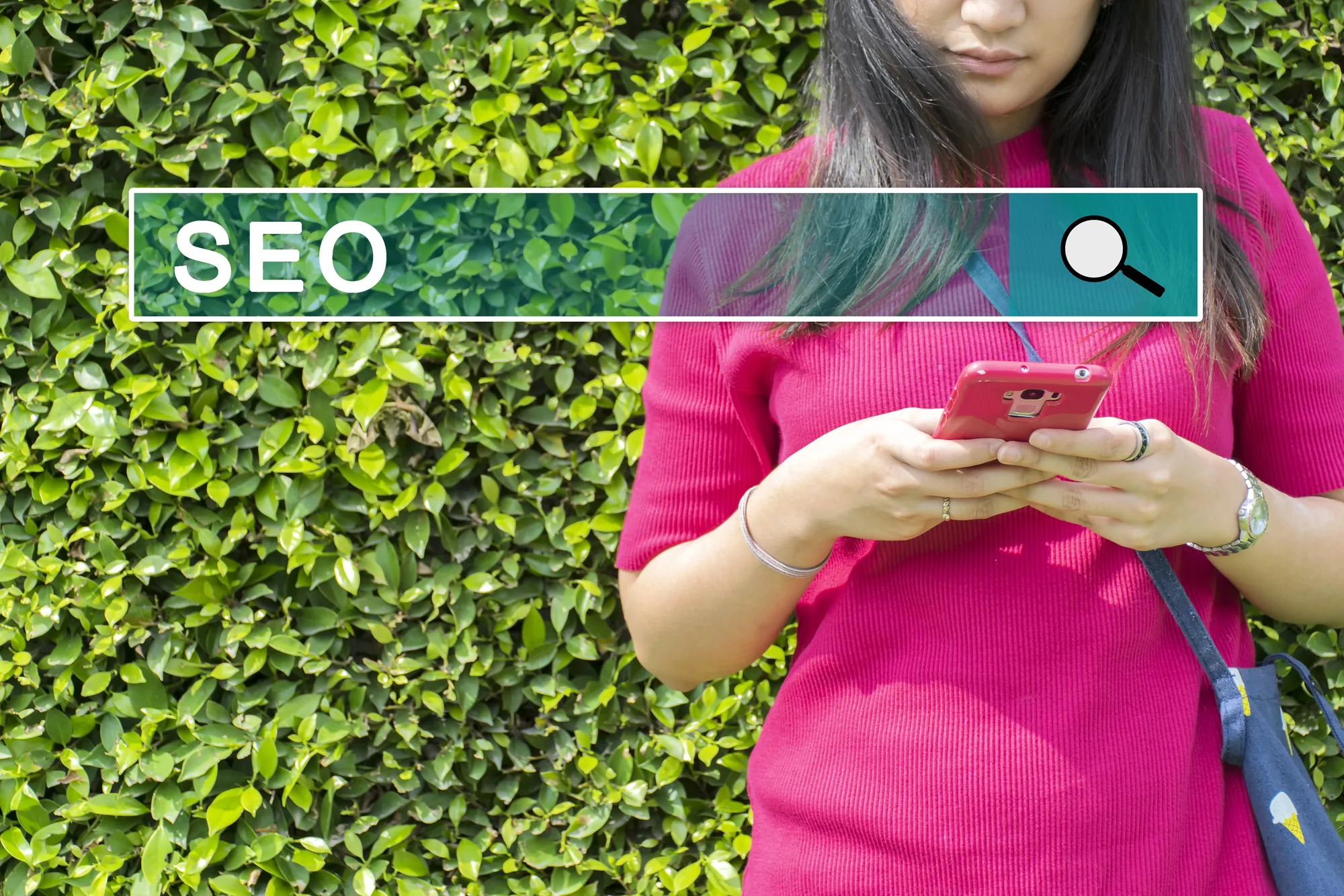 Woman using a smartphone in front of a hedge with an SEO search bar graphic overlaid on the image