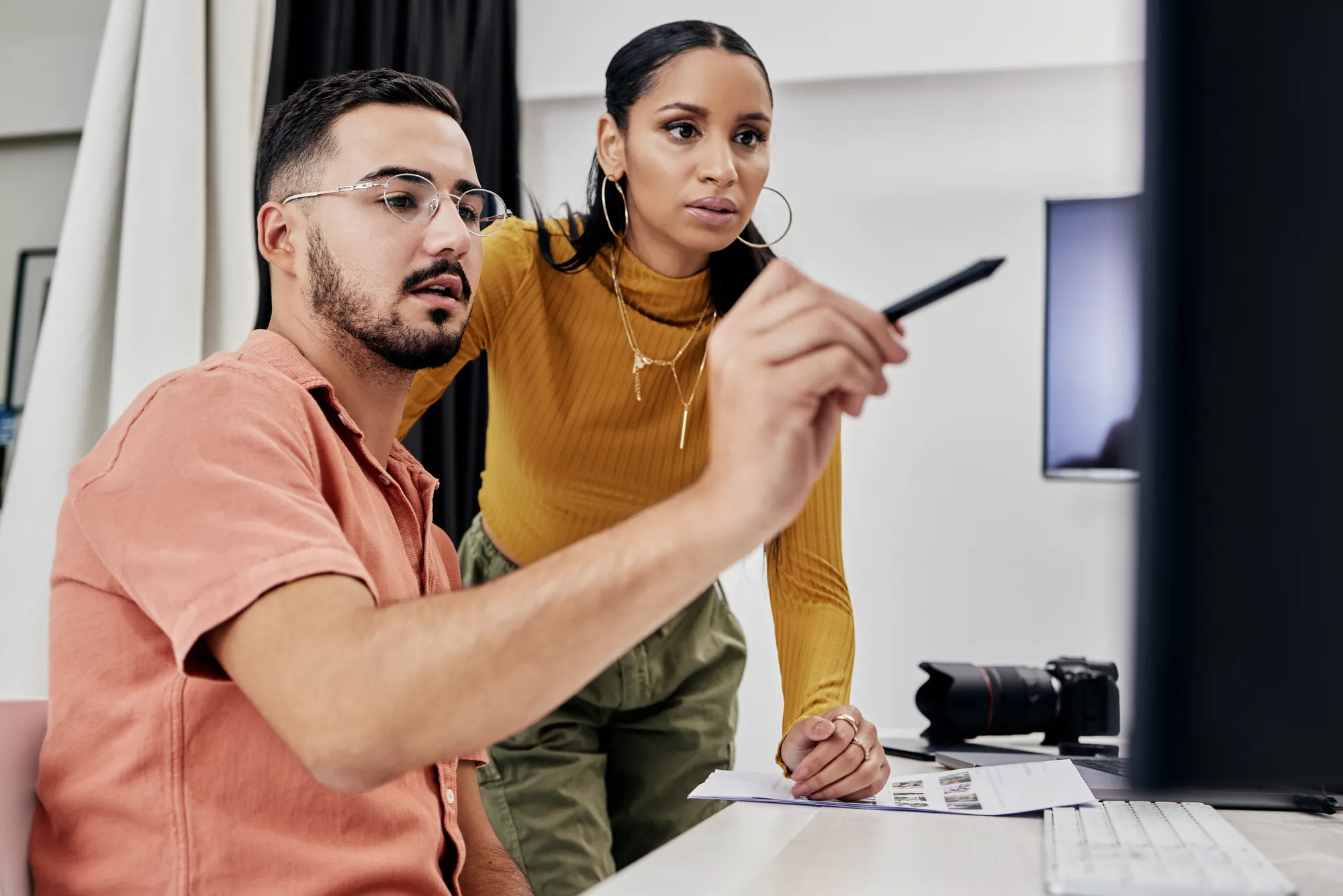 Two coworkers reviewing photo proofs together while looking at a computer screen in a creative studio