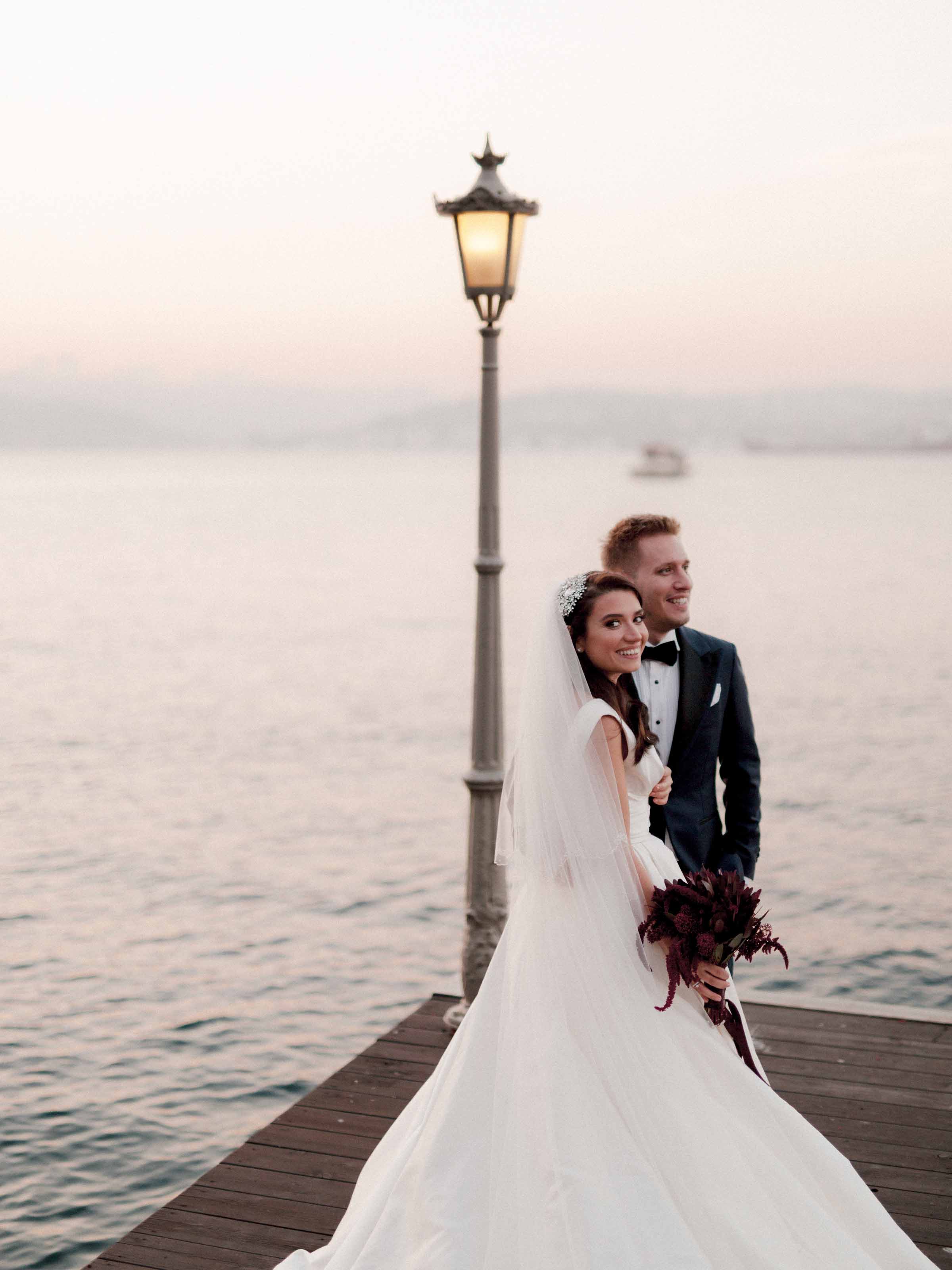 Bride and groom beside a lit lamppost on the waterfront pier at dusk, Cubuklu 29, Istanbul
