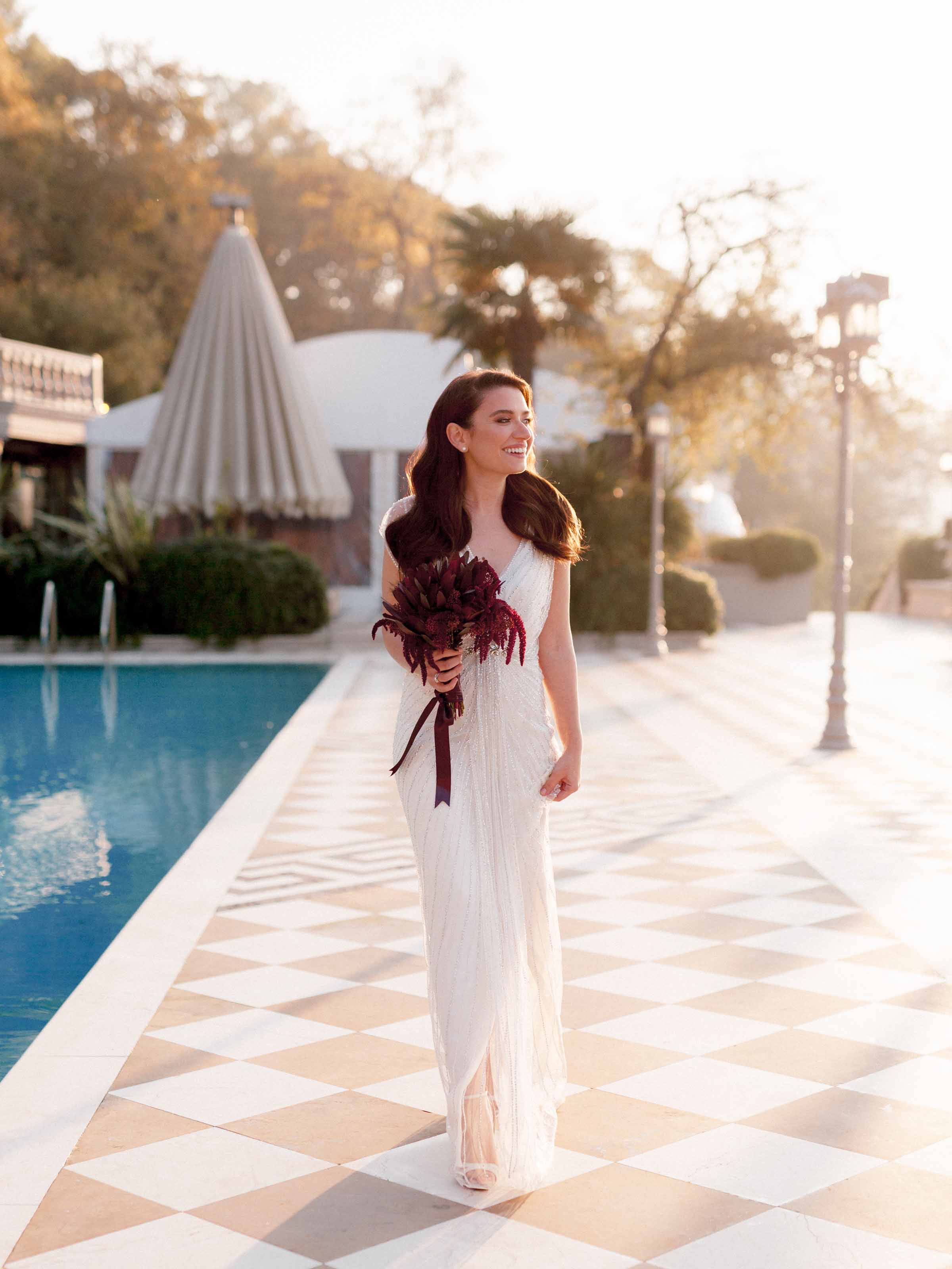 Bride with a deep red bouquet walking a poolside terrace at dusk, Cubuklu 29, Istanbul