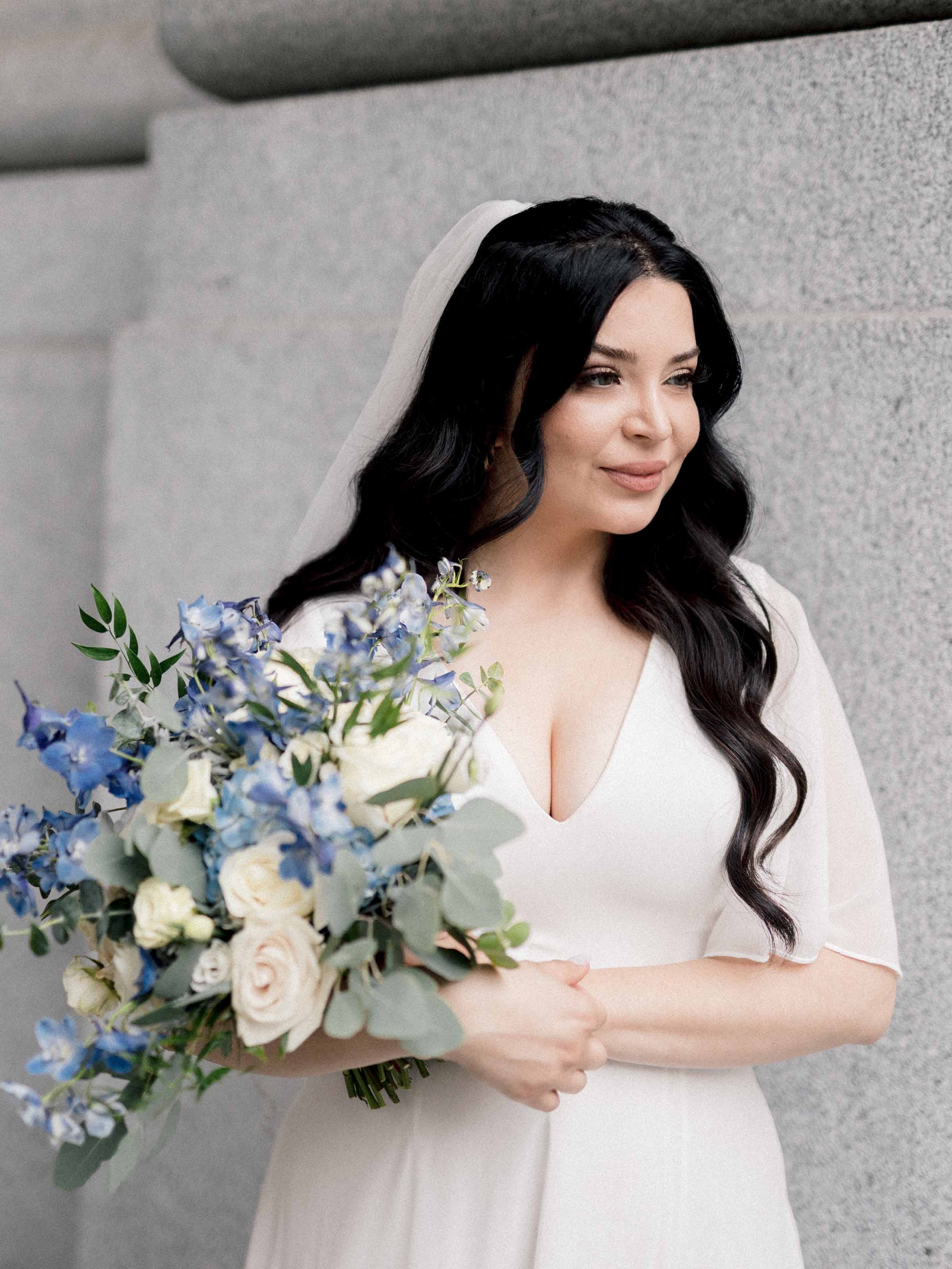 Mariée tenant un bouquet bleu et blanc devant un mur de pierre, Montréal