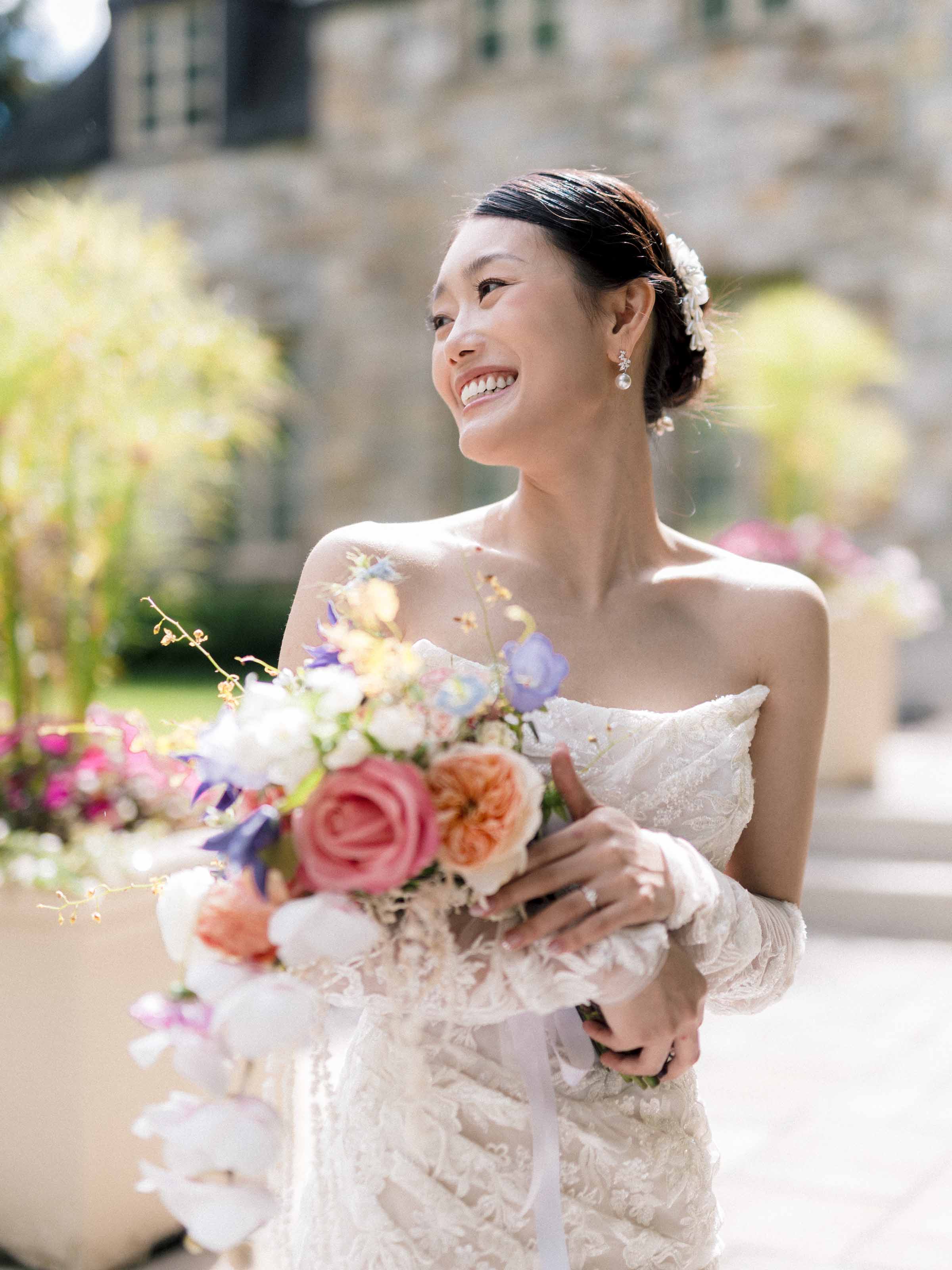 Mariée riant avec un bouquet coloré devant un lieu en pierre