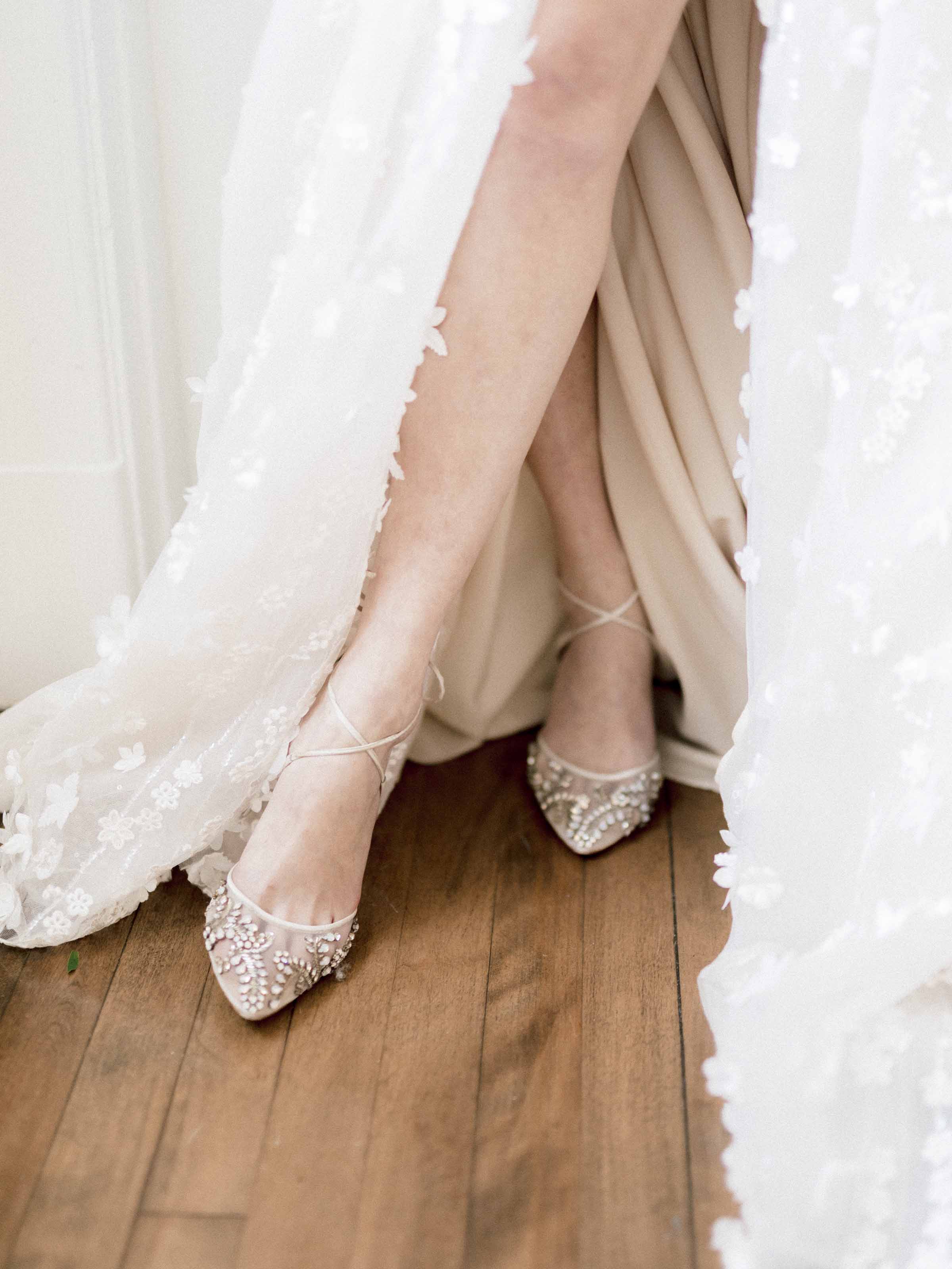 Bride's crystal-embellished heels beneath an embroidered floral gown on a wood floor, Montréal