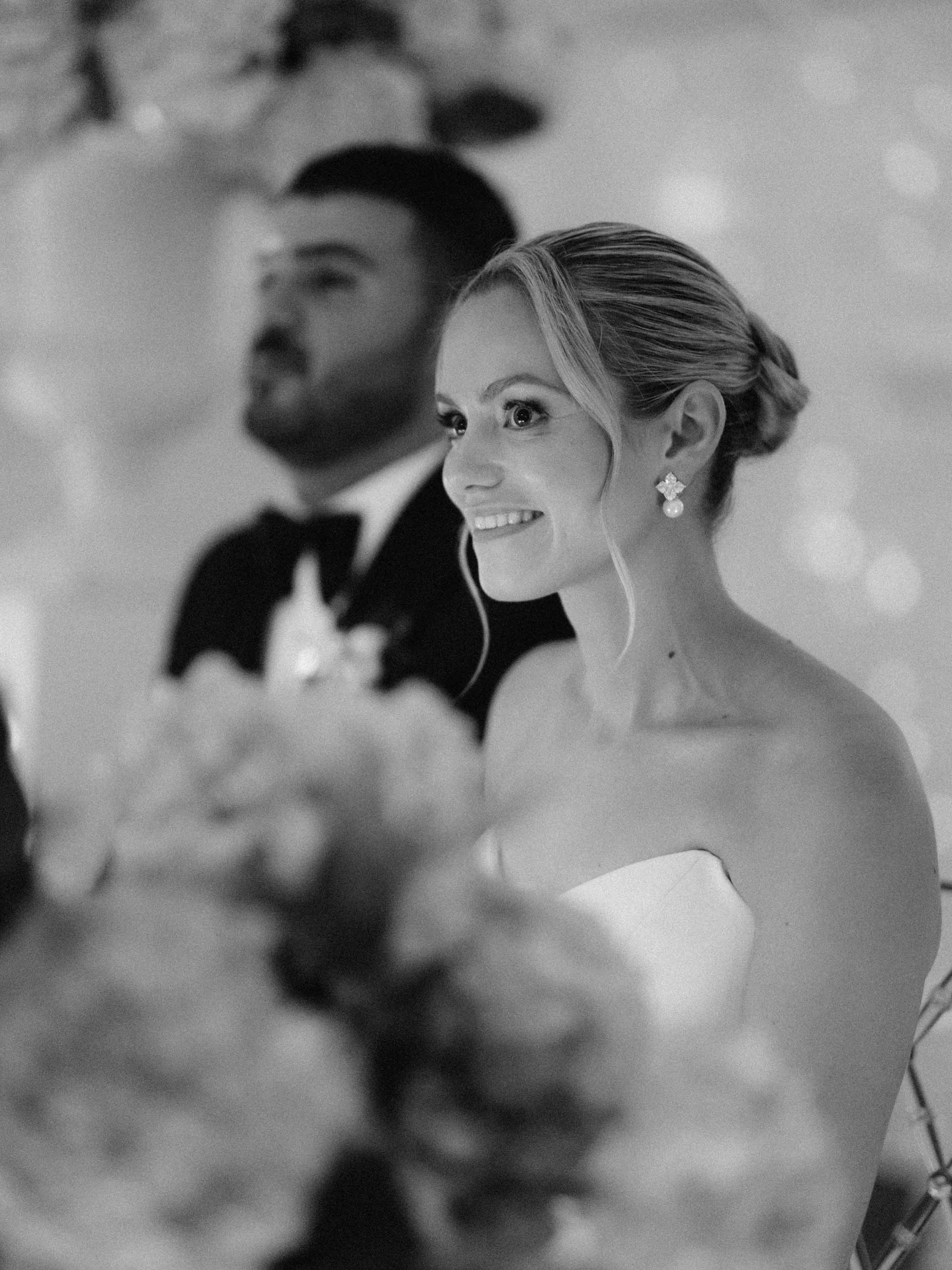 Mariée souriante aux côtés du marié derrière un écran de fleurs, noir et blanc, Montréal