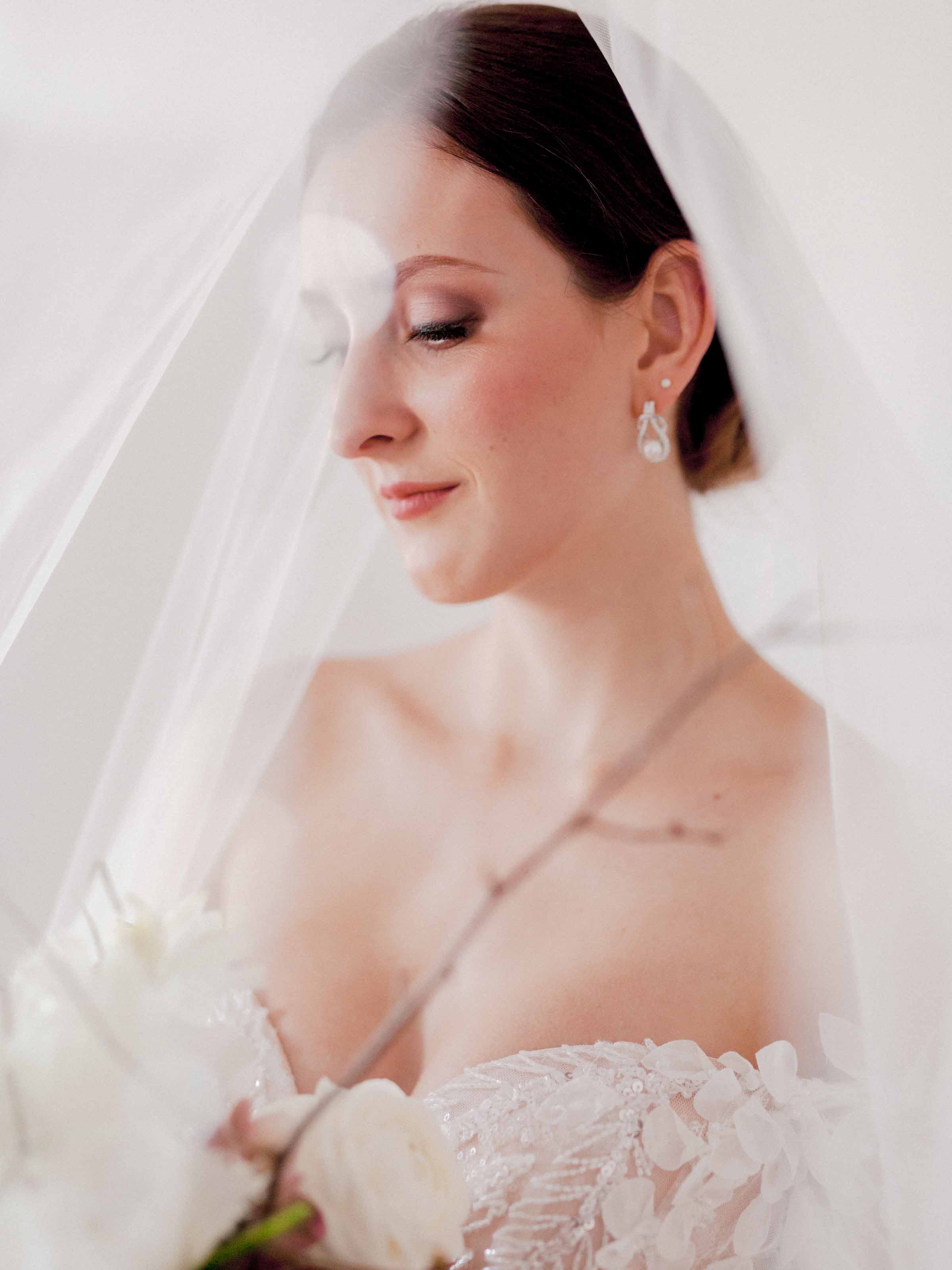 Bride beneath a sheer veil with a pearl drop earring and white roses, Québec City