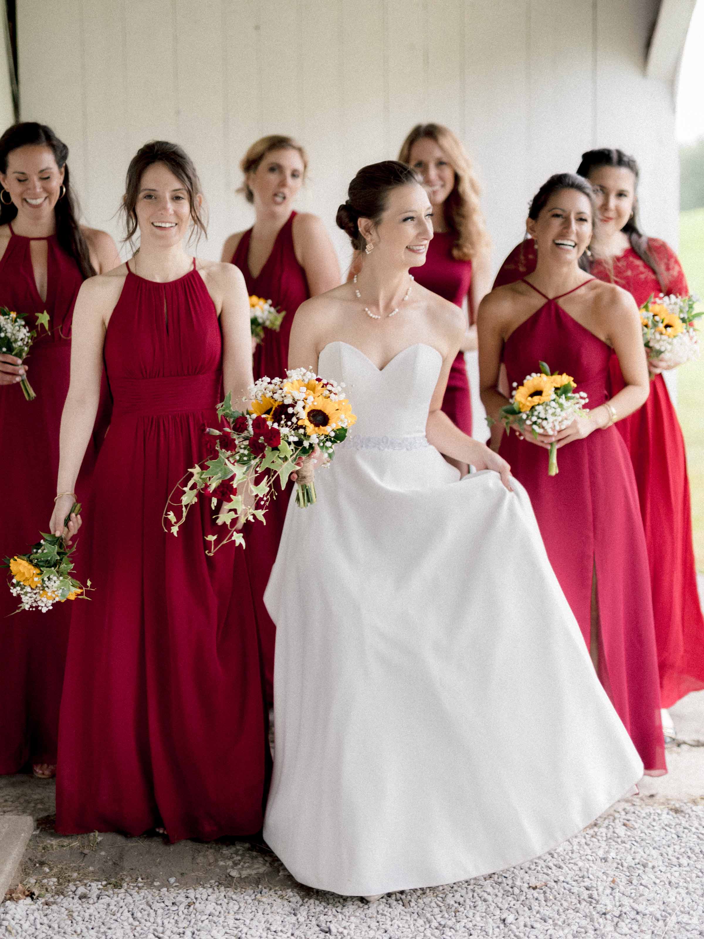 La mariée et ses demoiselles d'honneur en rouge foncé, portant des bouquets de tournesols