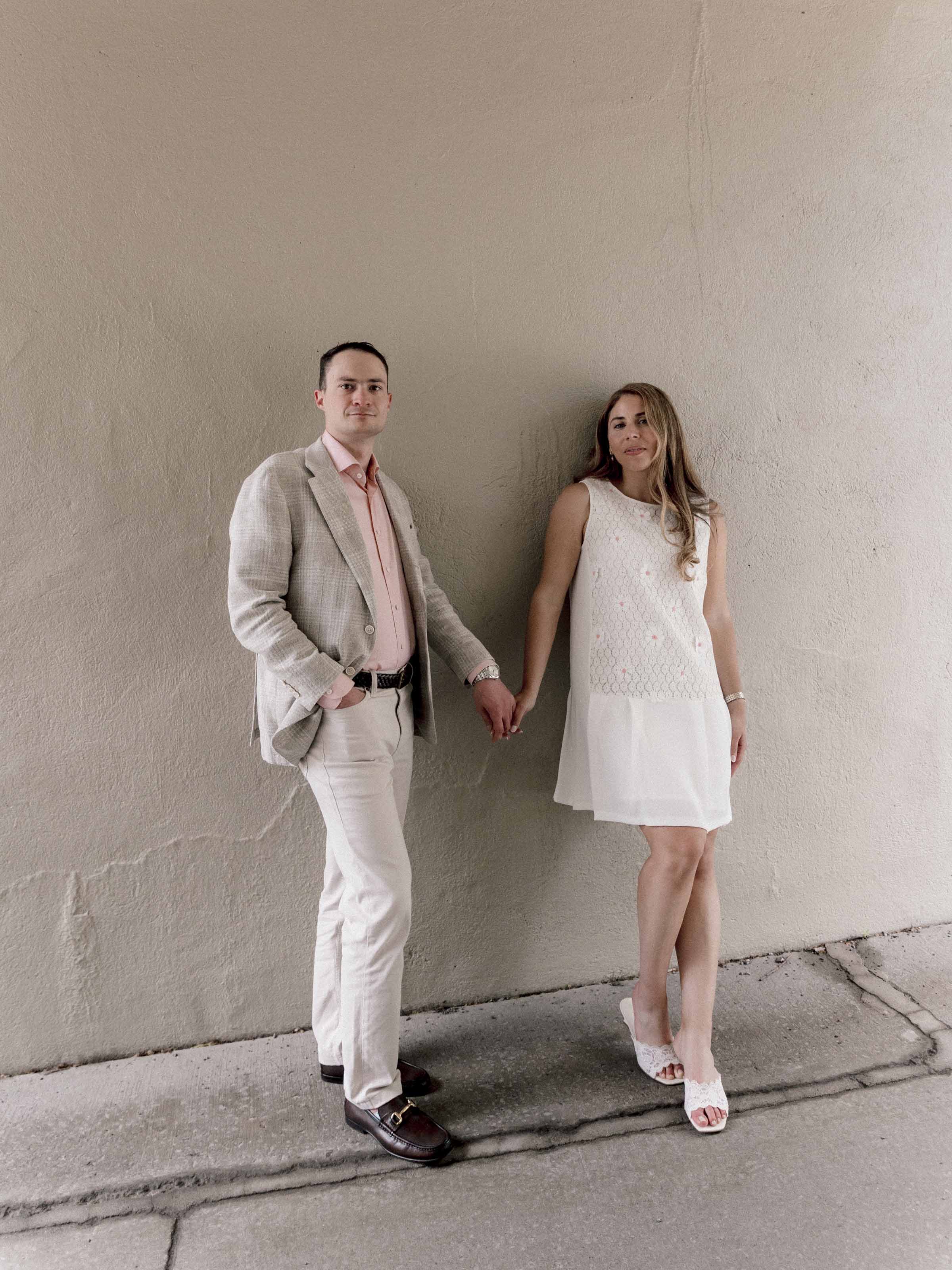 Engaged couple holding hands against a pale concrete wall, Québec City
