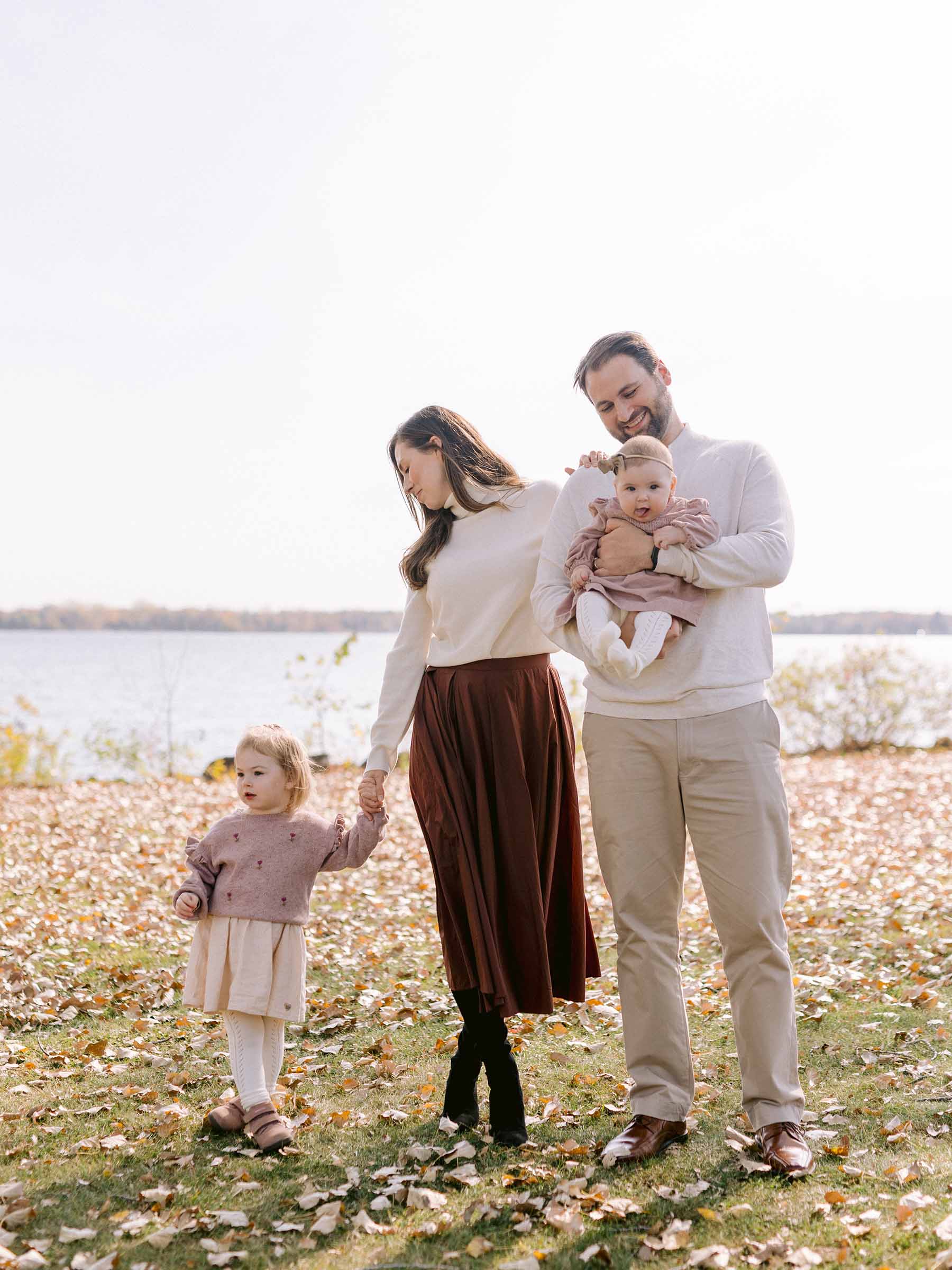 Parents walking through fallen leaves beside the water with their toddler and baby on an autumn afternoon, Montréal