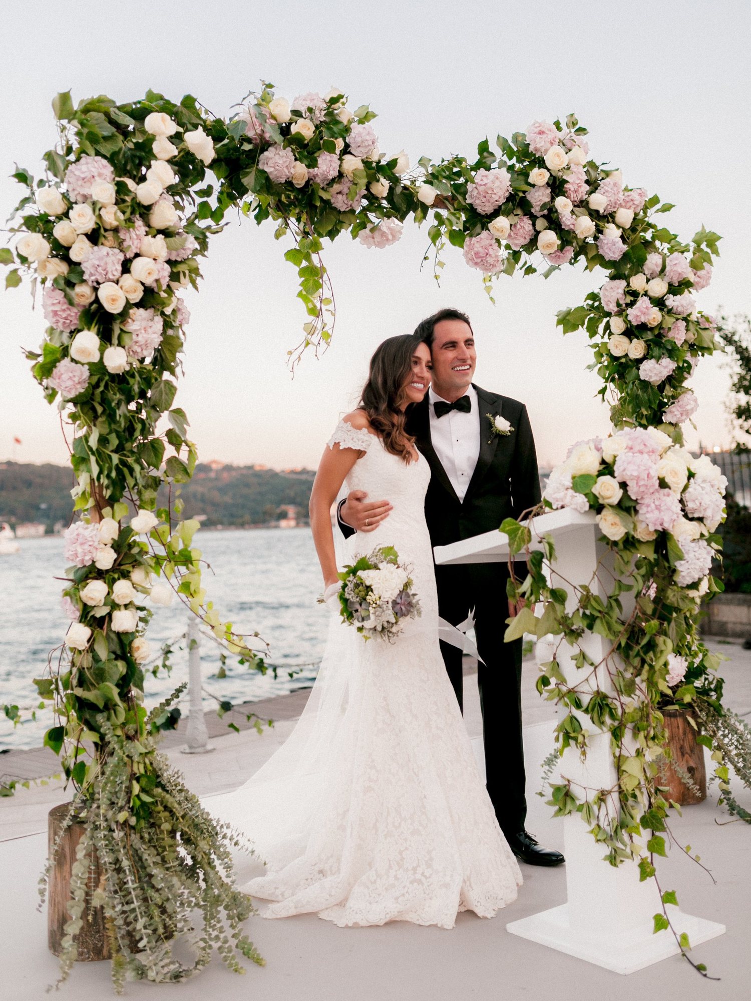 Bride and groom beneath a floral arch of roses and hydrangeas on the Bosphorus waterfront in Istanbul